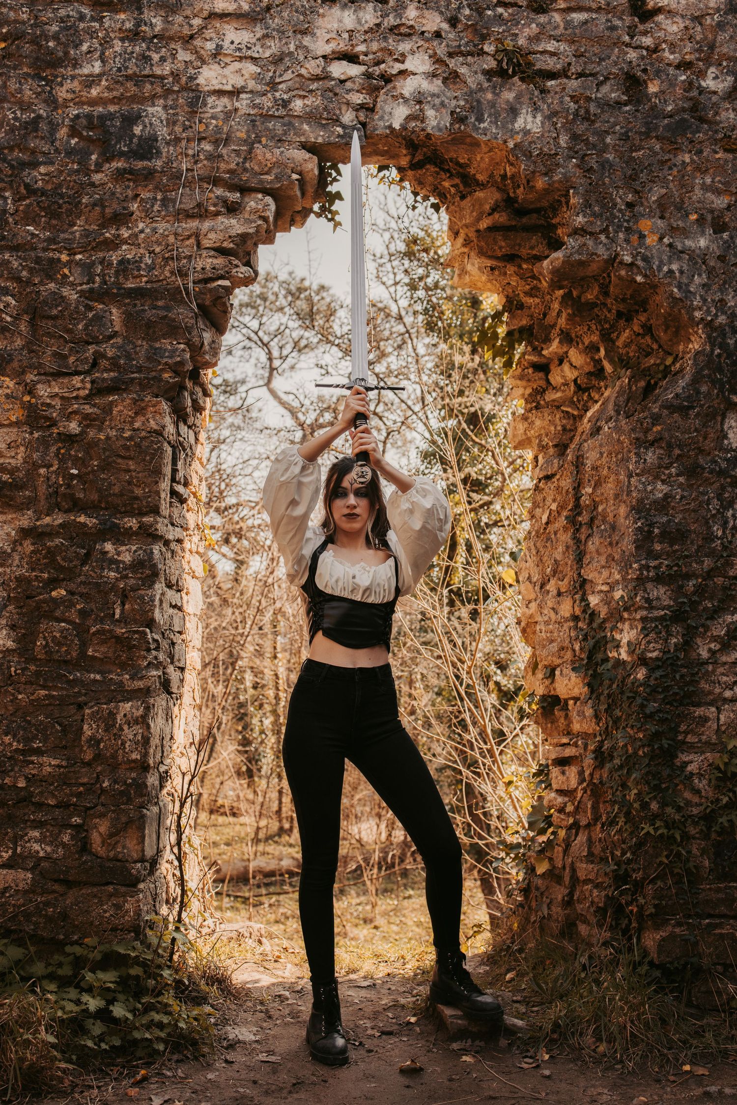 A warrior poses with raised sword in stone archway with dramatic lighting.