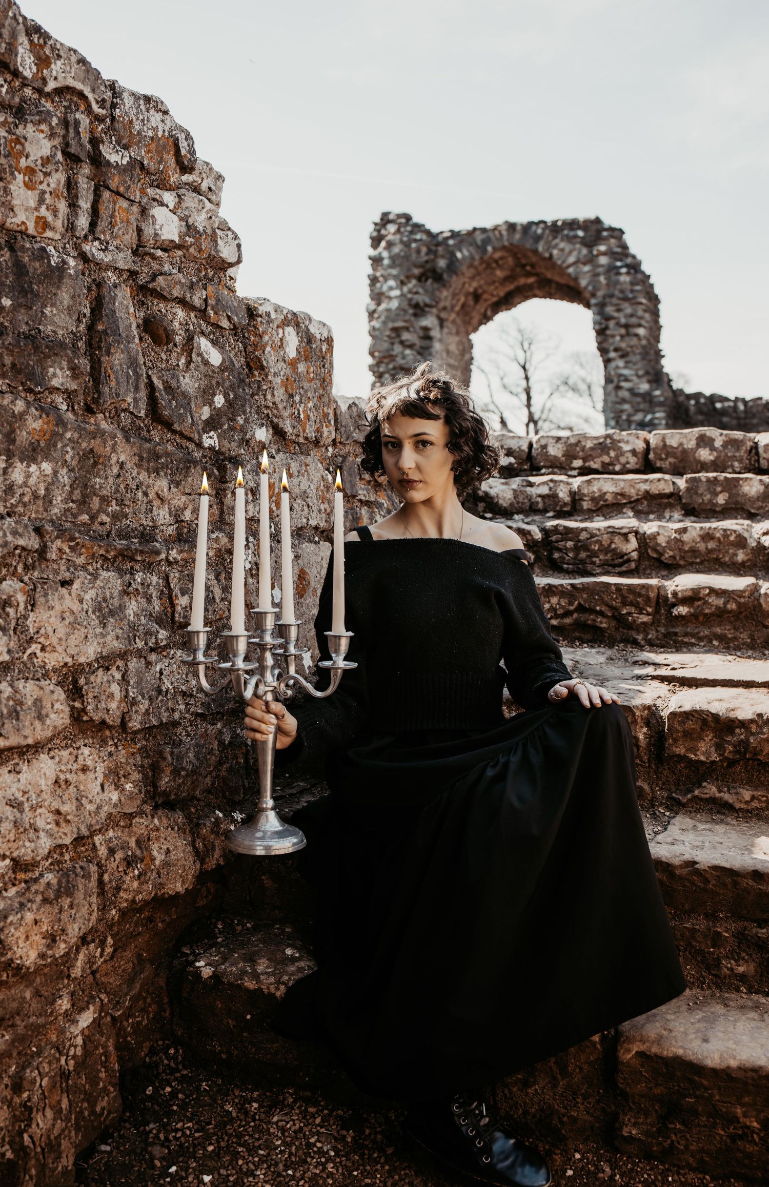 Dramatic portrait series against stone ruins with silver candelabra and black dress.