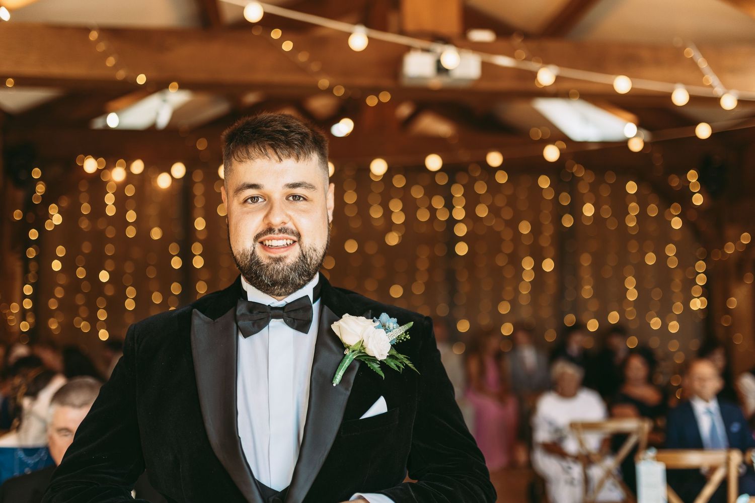 A romantic wedding reception venue decorated with warm string lights and elegant table settings in a rustic indoor space.