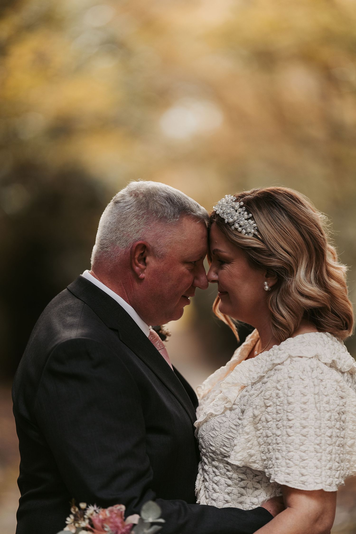 An intimate moment between a couple in formal attire against an autumn backdrop.