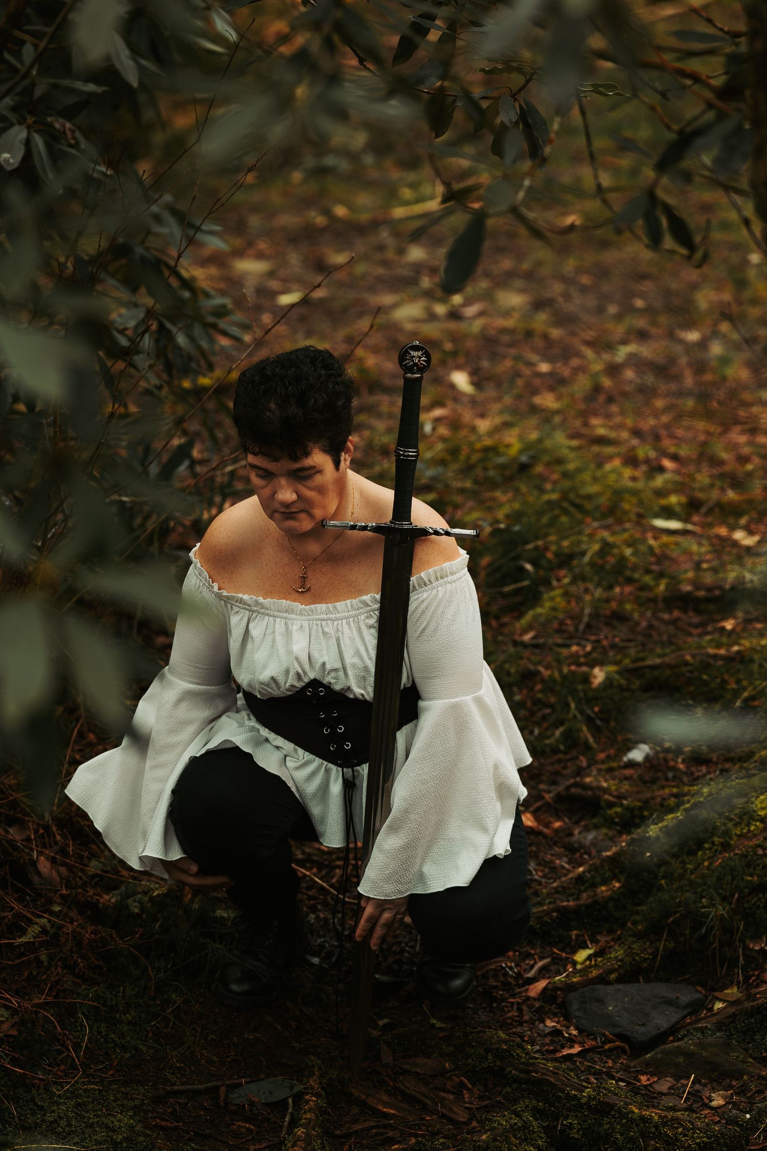 Atmospheric forest scene with off-shoulder white blouse and dark styling.