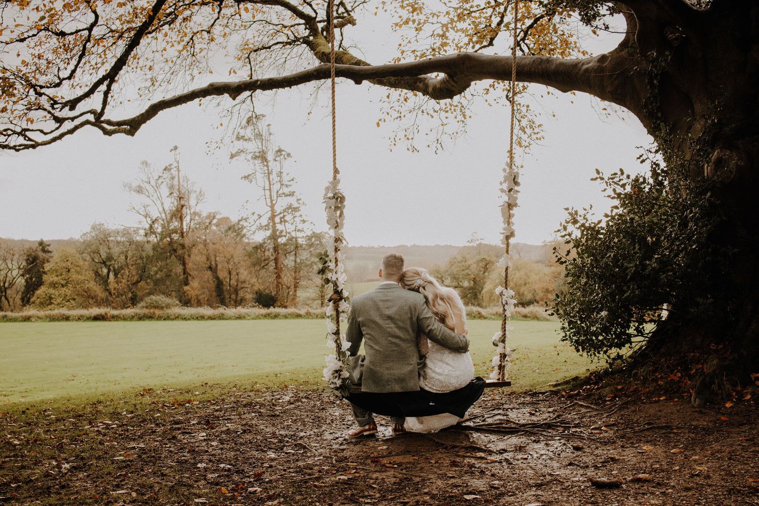 A couple enjoying a romantic moment on a tree swing in a pastoral setting.