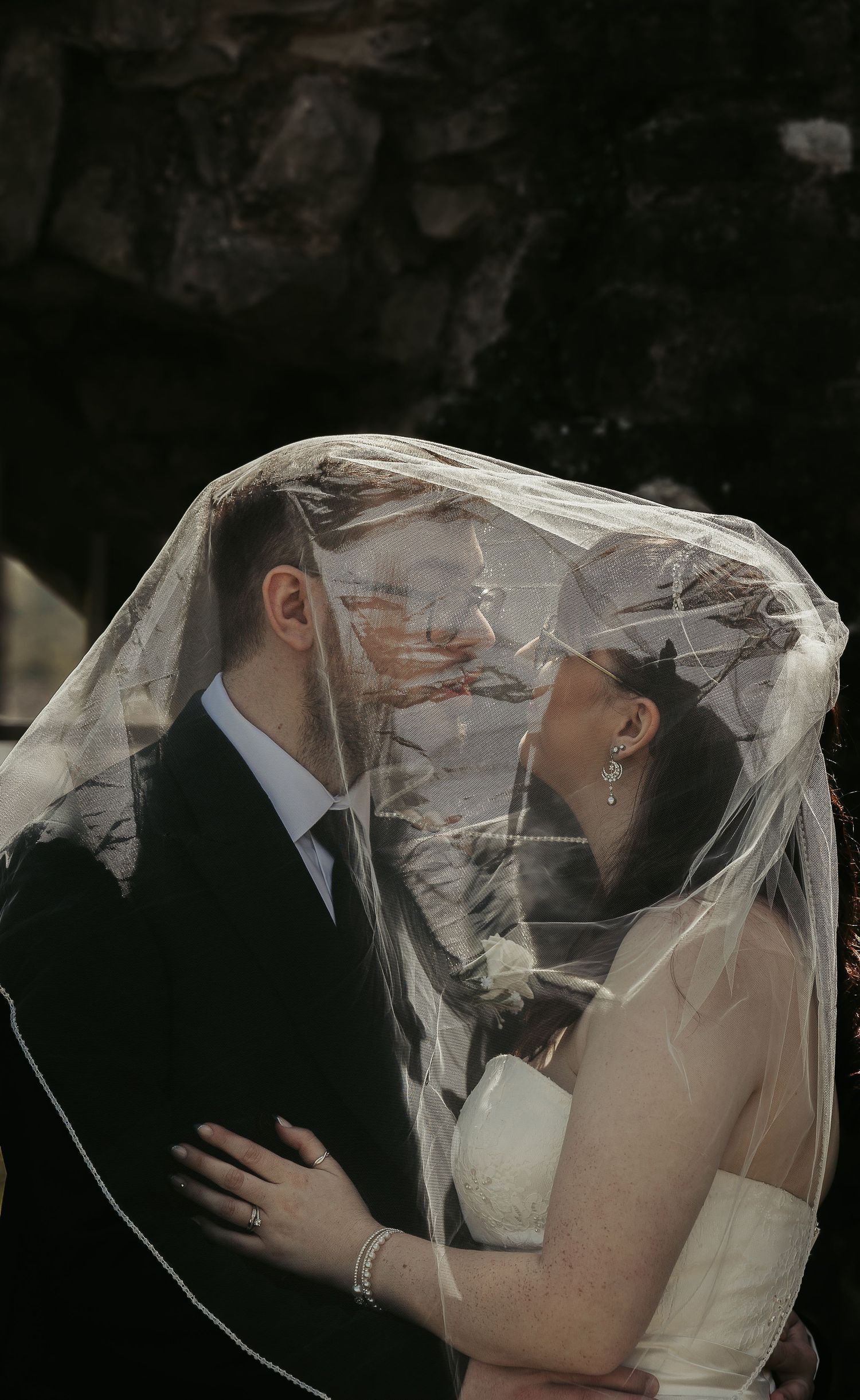 A bride and groom share an intimate moment under a sheer wedding veil, gazing at each other lovingly.