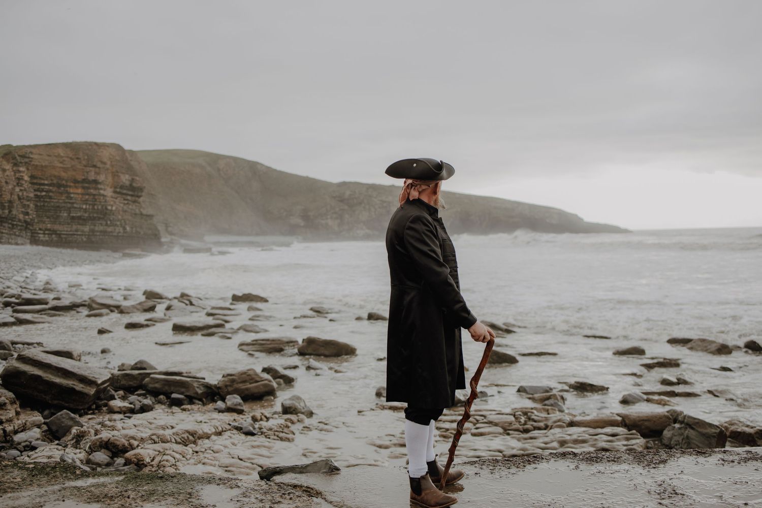 Figure in dark clothing walking along a misty rocky coastline.
