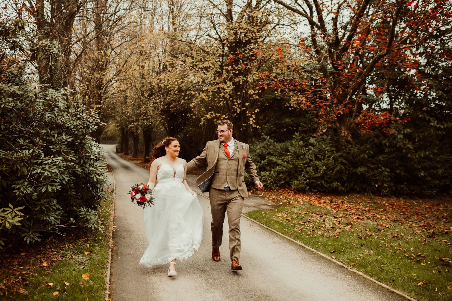 A joyful couple runs down an autumn path surrounded by colorful fall foliage.