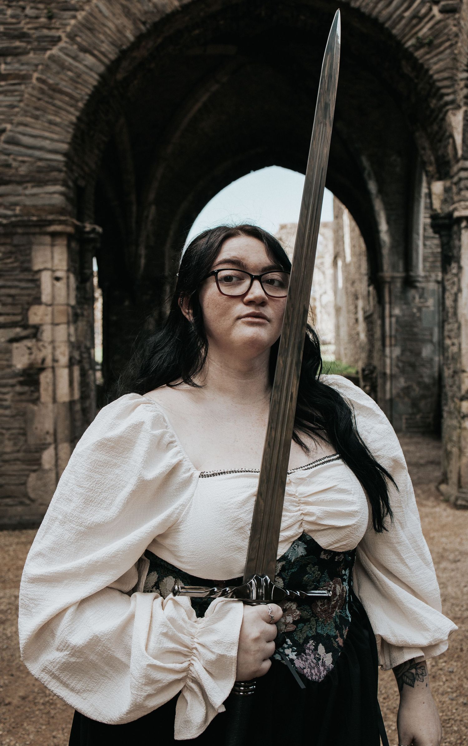 A warrior poses with a sword in a historic stone archway setting.