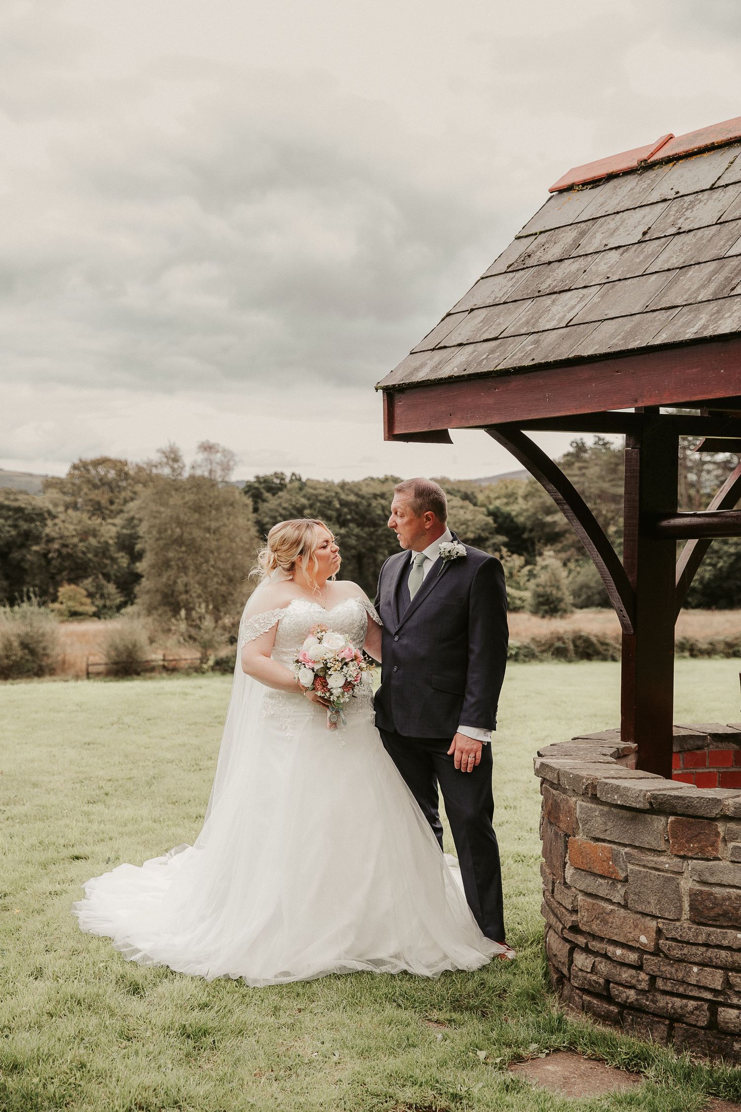 Rustic wedding portraits taken by a charming stone well house in a pastoral countryside setting.