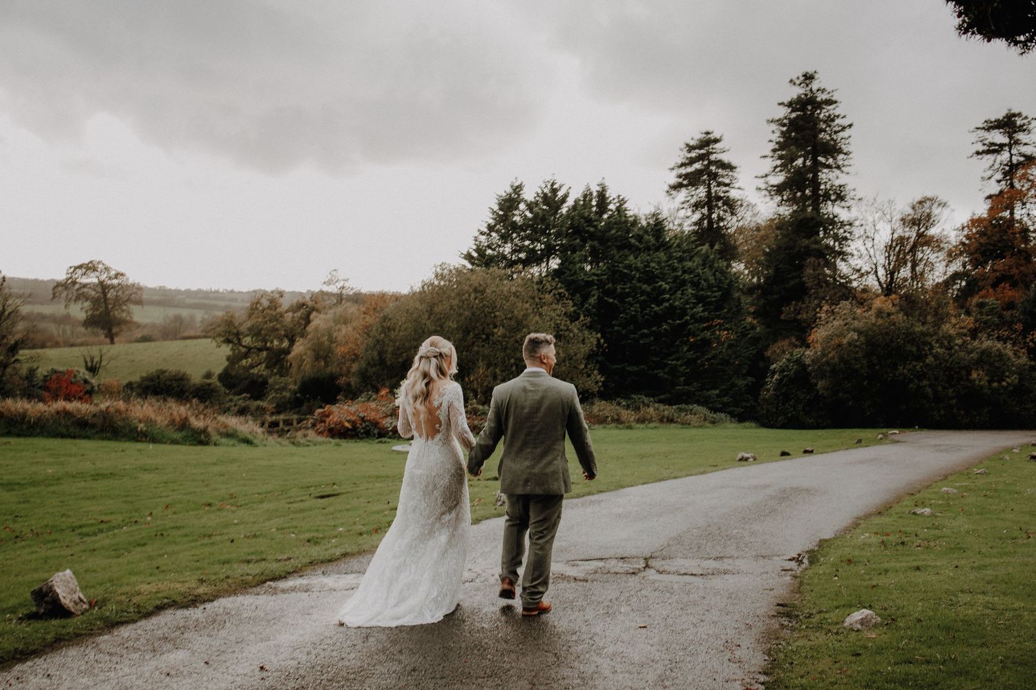 Couple walking down a winding path through scenic countryside on their wedding day.