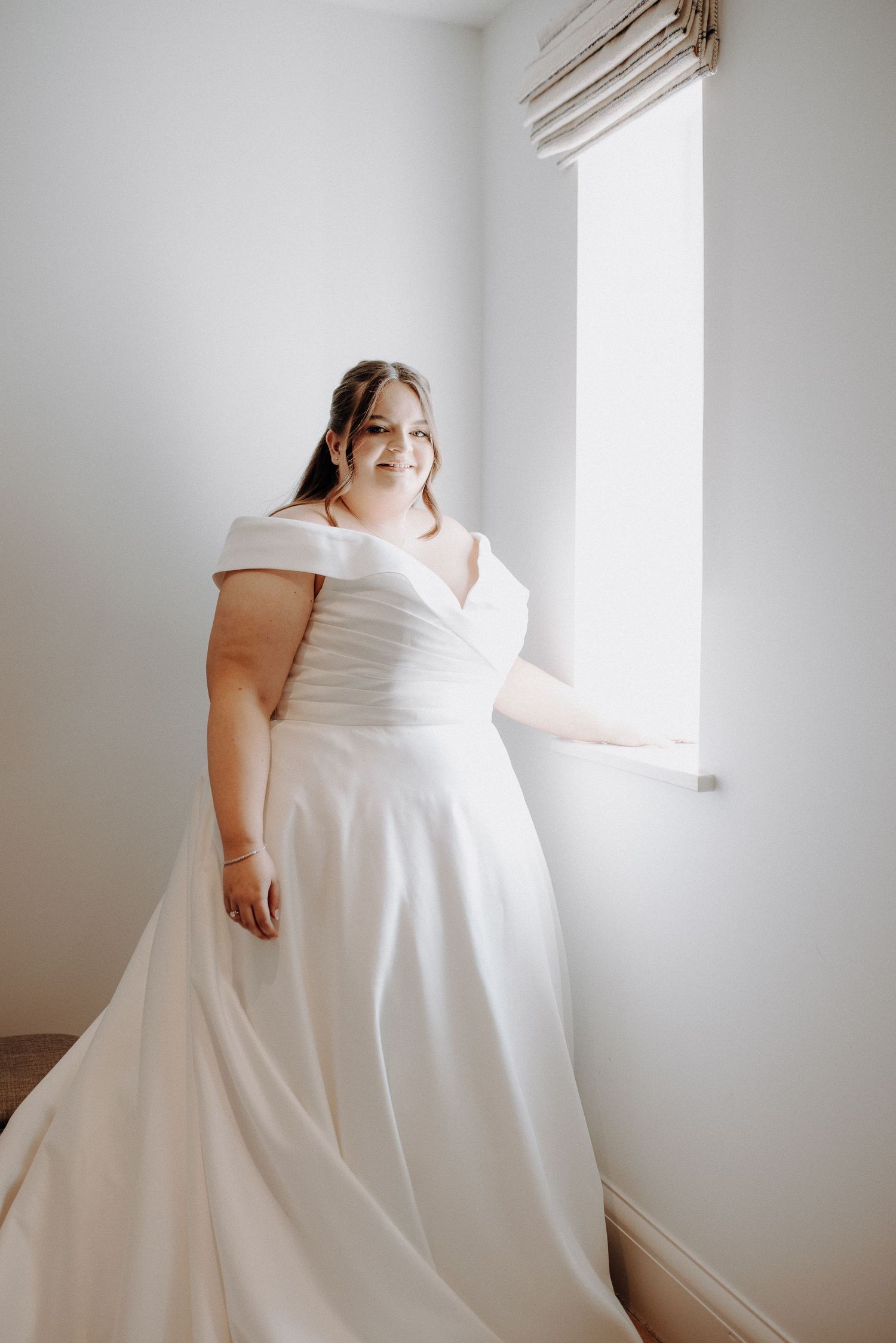Elegant white wedding dress photographed in a bright minimalist room with natural lighting.