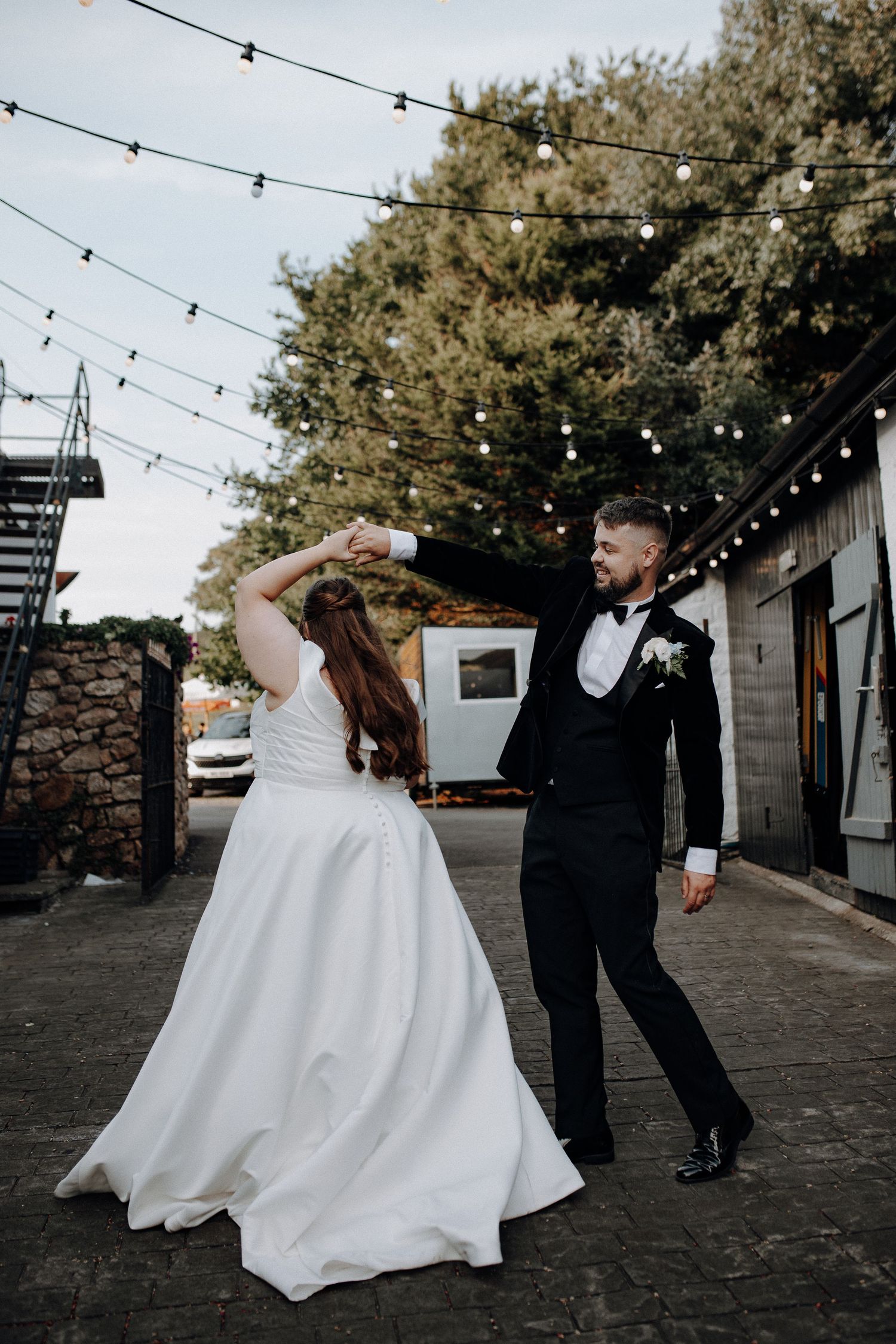 A couple dances together under string lights at their wedding reception on a stone patio.