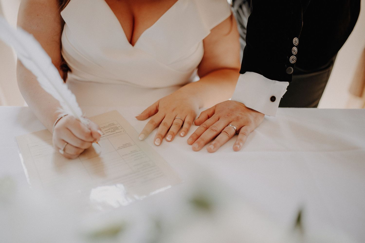 Close-up view of newlywed couple's hands during marriage document signing ceremony at white table.
