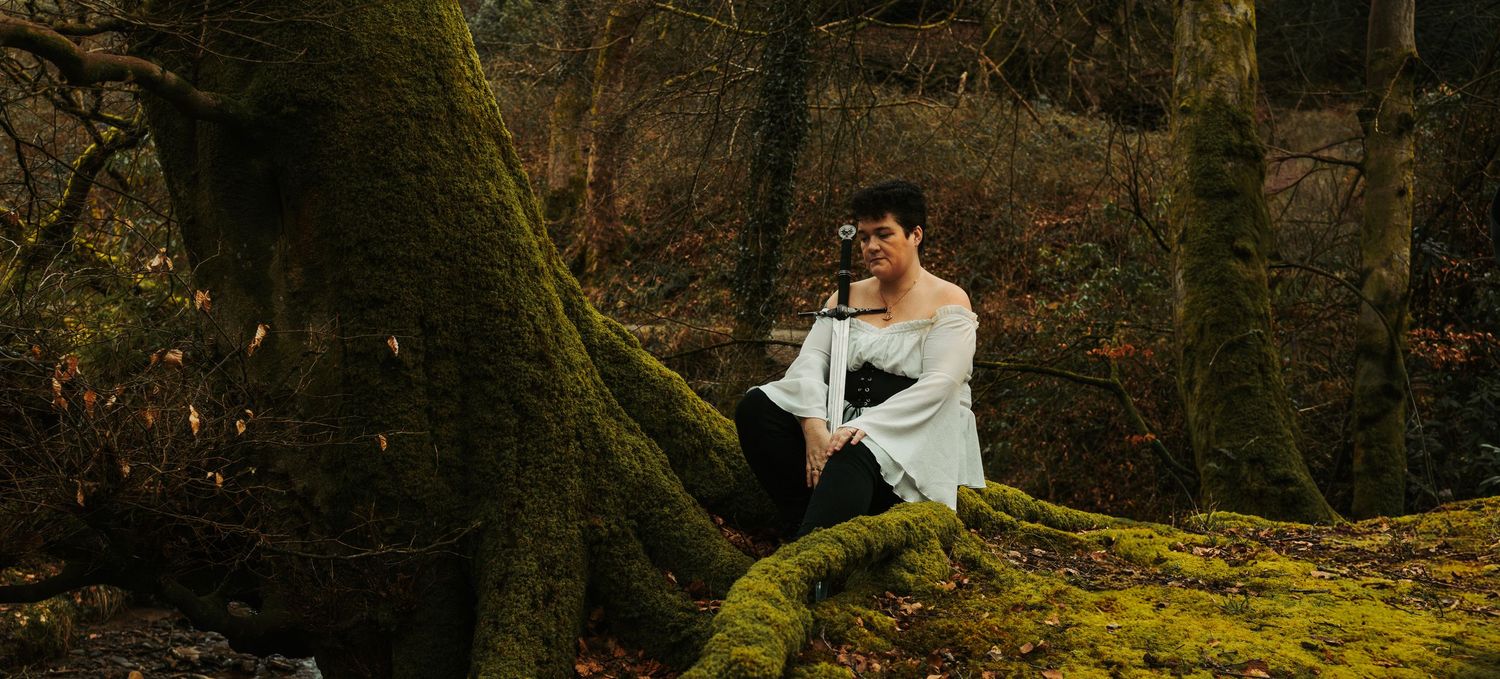 Woman in white dress sits on moss-covered tree roots in an enchanted autumn forest setting.