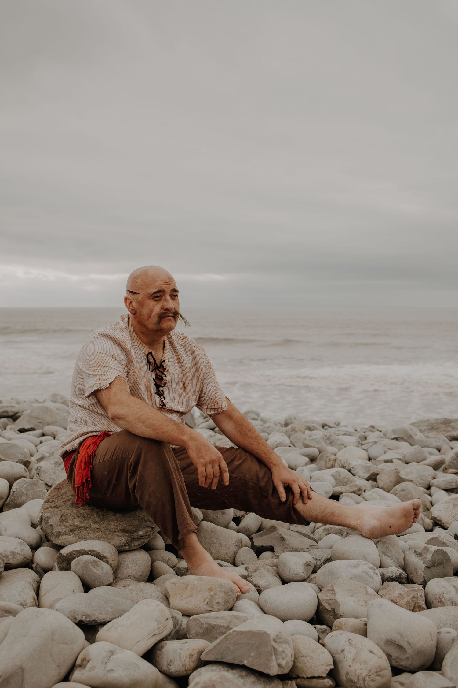Person in pirate costume sitting thoughtfully on large coastal rocks by the ocean.