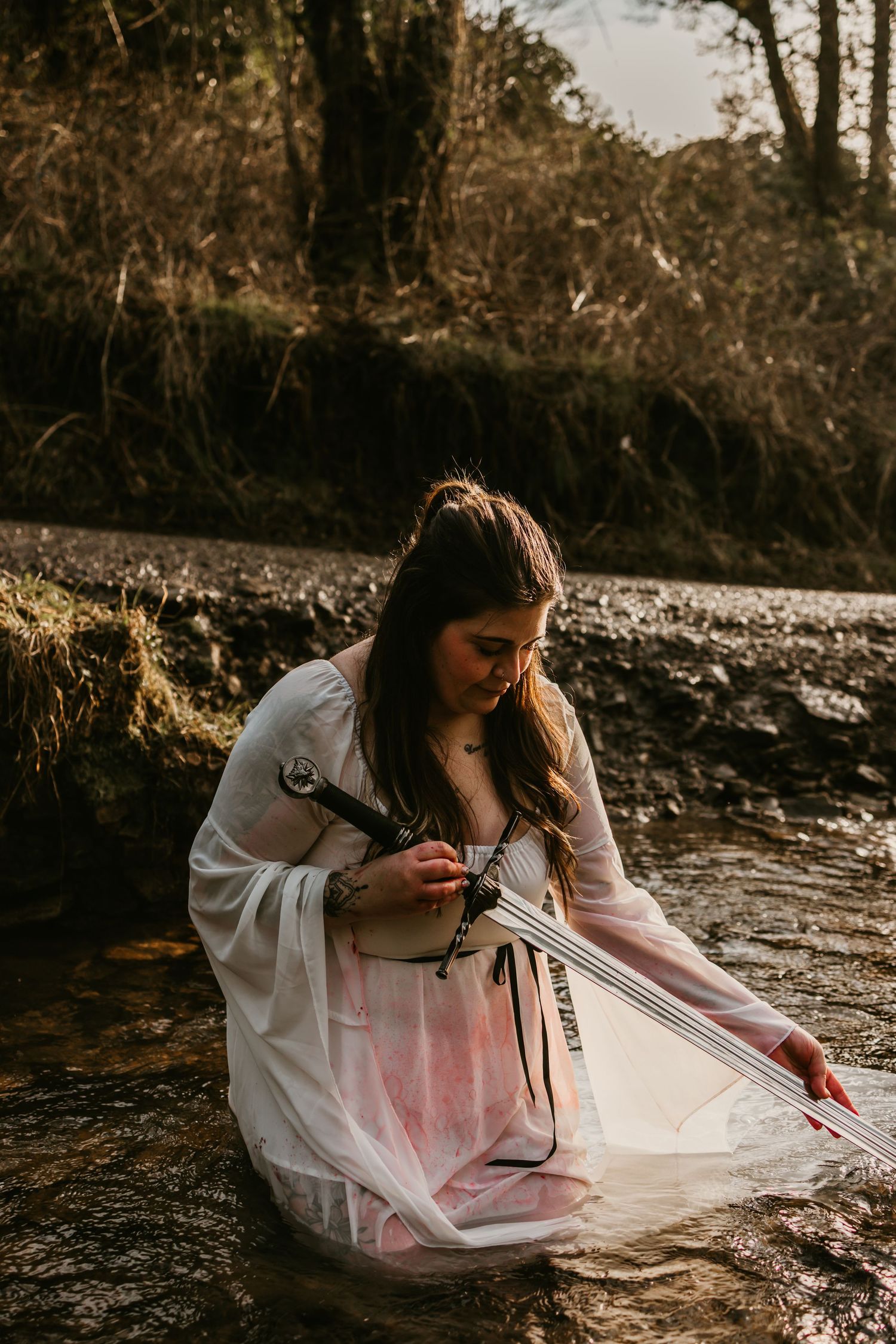 Person in white dress reclining on rocky ground in ethereal forest setting.