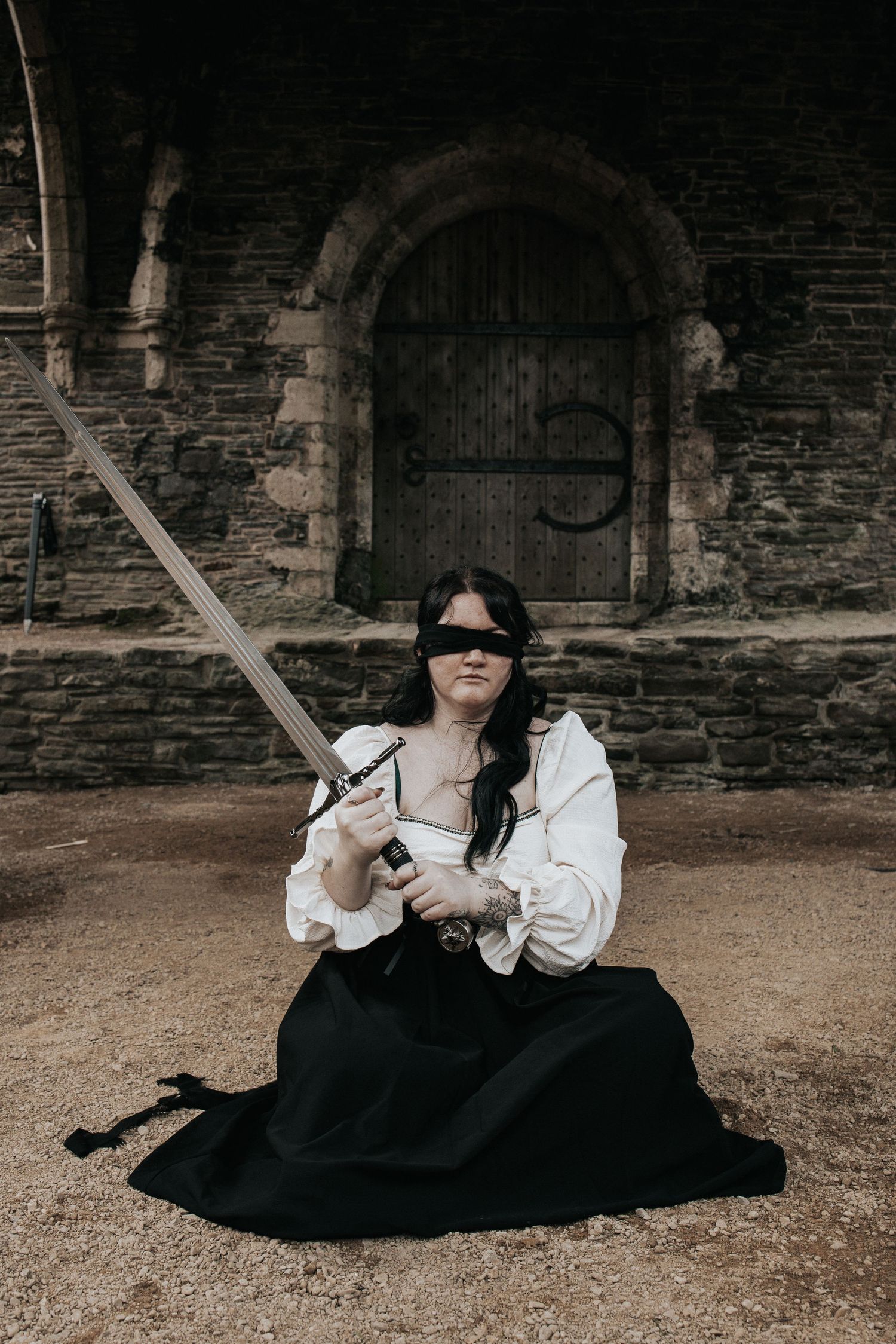 A figure in renaissance attire poses with sword against stone architecture.