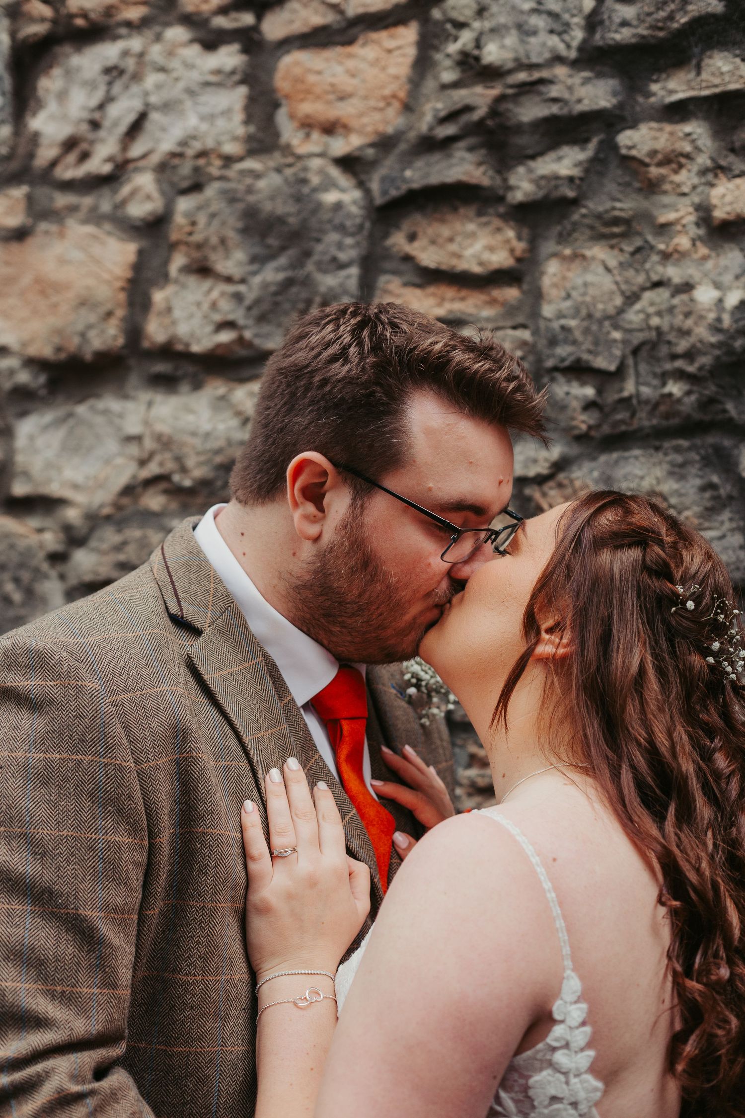 A romantic wedding moment captured against a rustic stone wall backdrop.