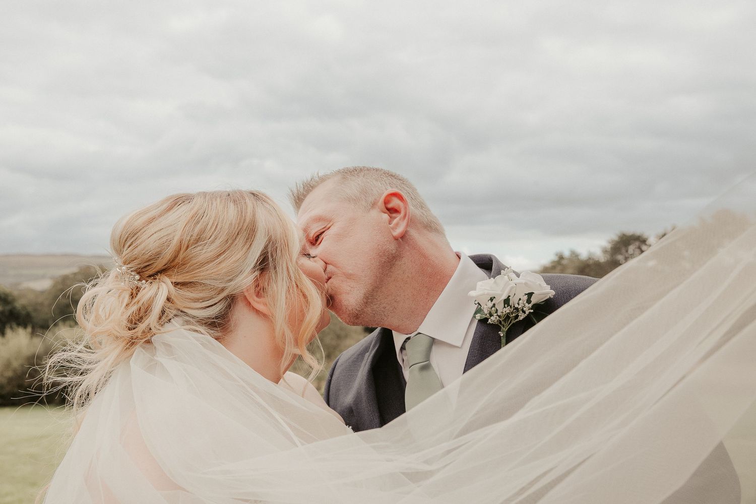 Romantic wedding portraits with flowing veil against soft cloudy sky.