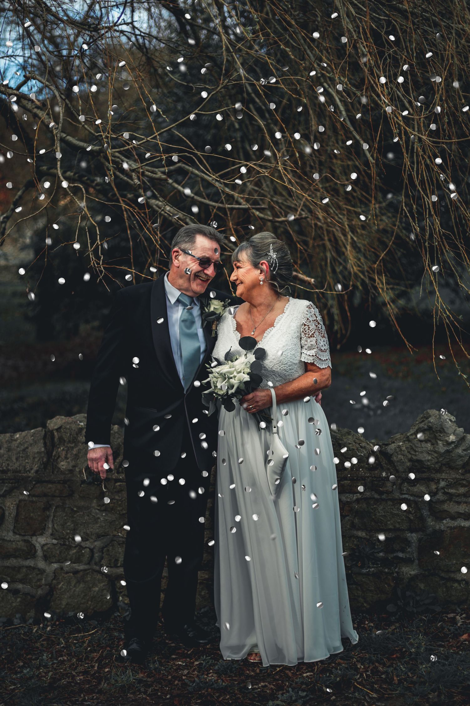 Romantic winter wedding photo with falling snow and twinkle lights creating magical atmosphere.