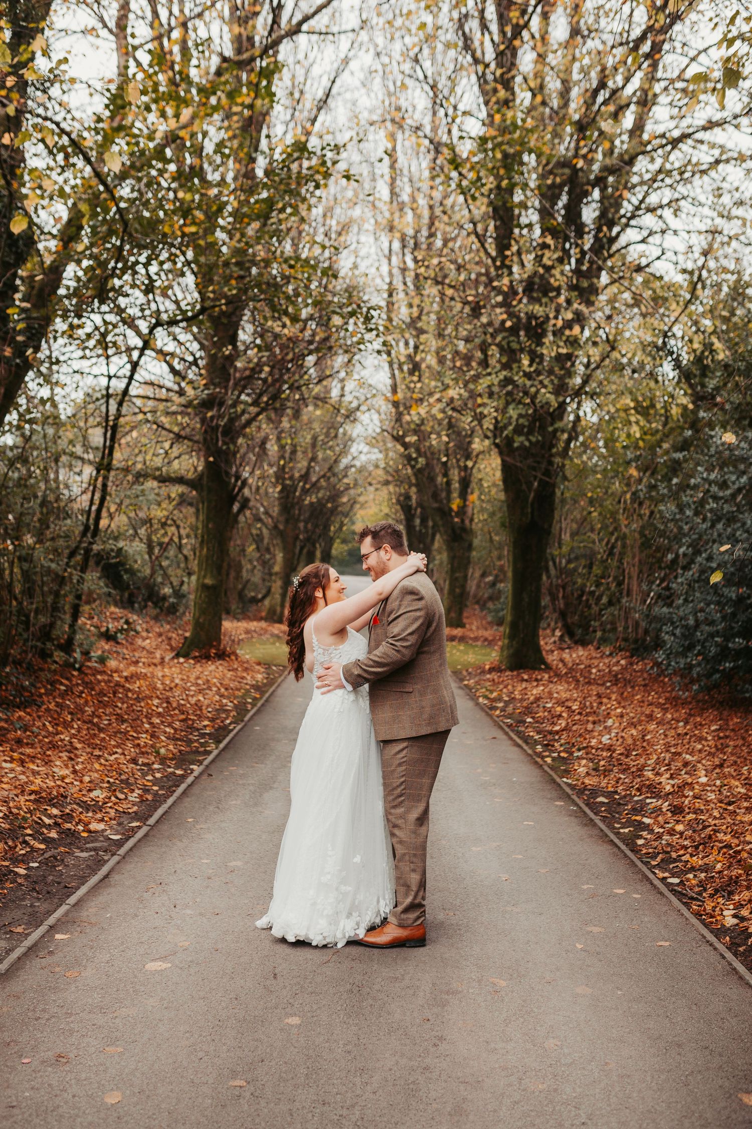 A romantic autumn wedding photo series on a path surrounded by fallen leaves.