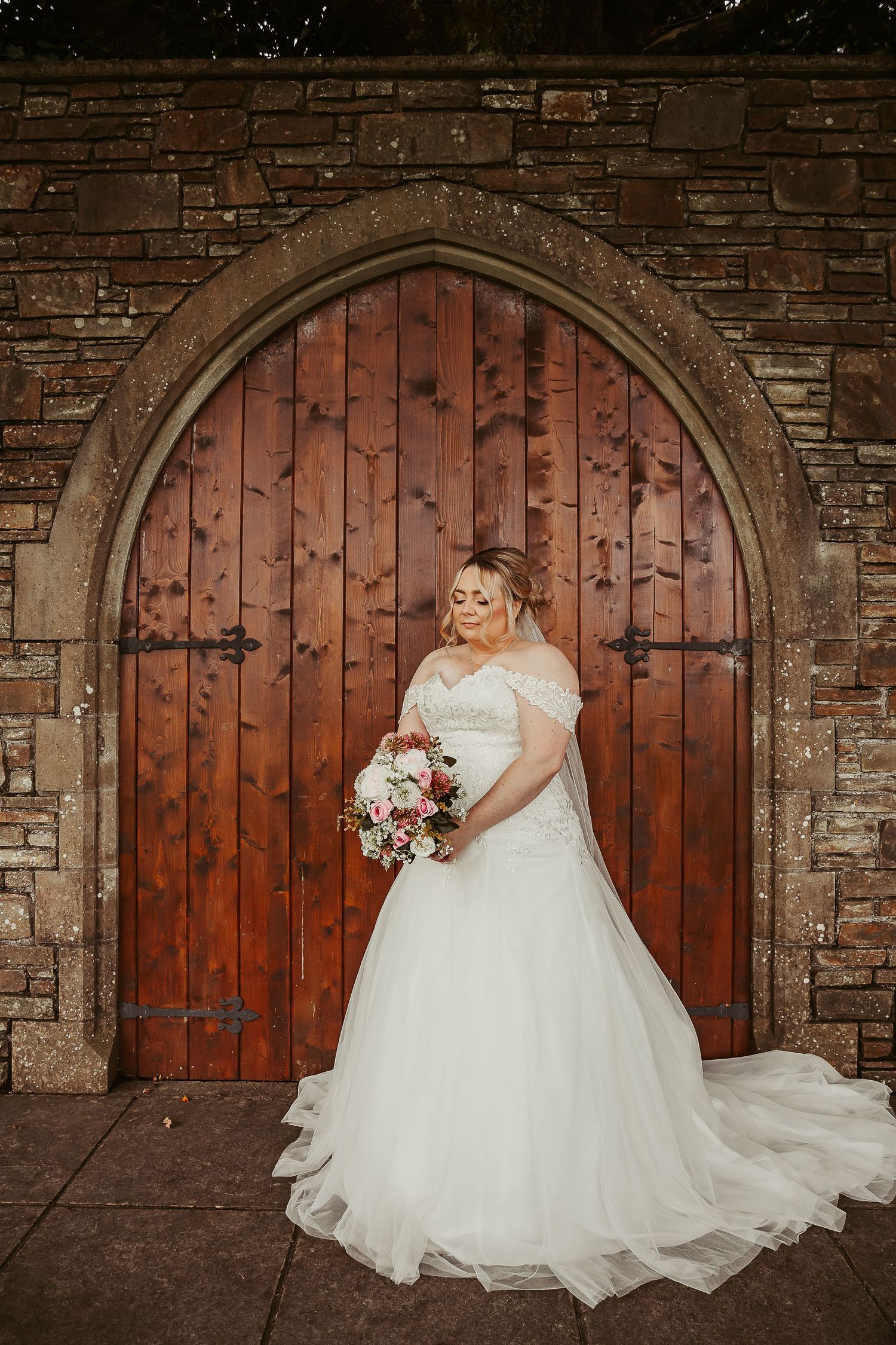 Wedding portraits against rustic wooden arched doors with stone brick walls.