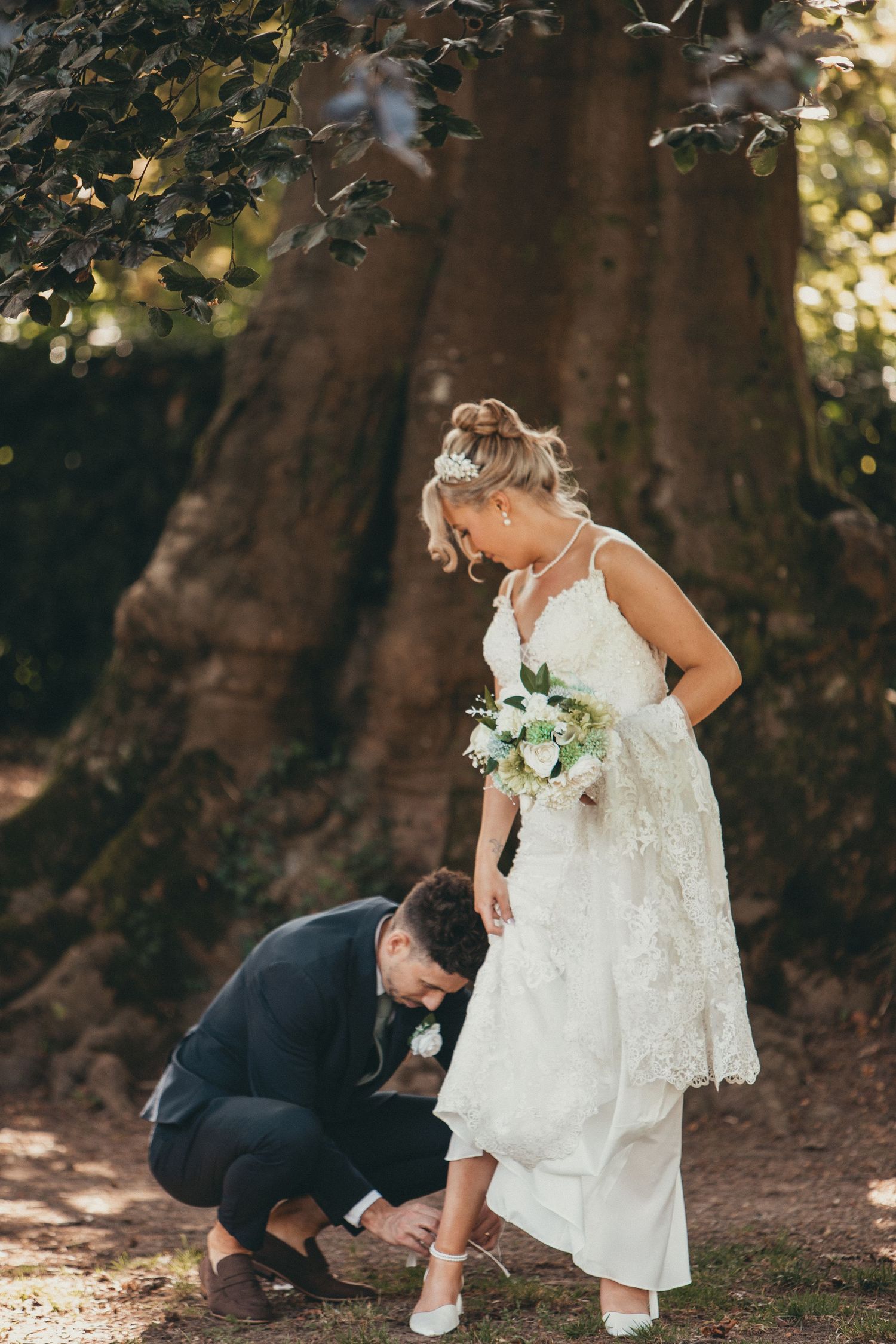 Couple shares intimate moment under large trees during wedding photoshoot.