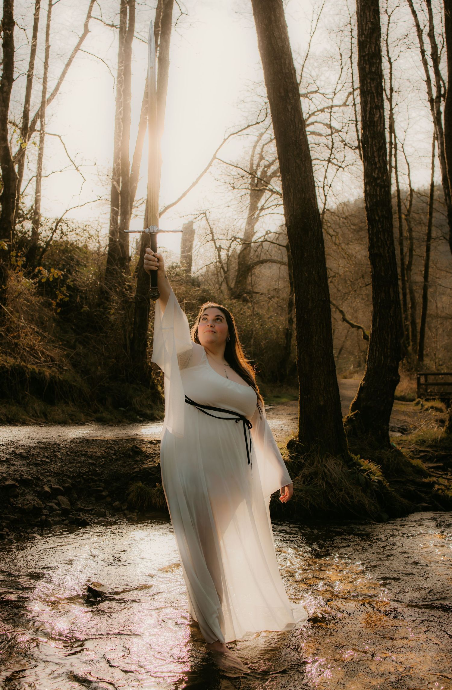 Dreamy forest scene with flowing white dress and mystical sunlight filtering through trees.