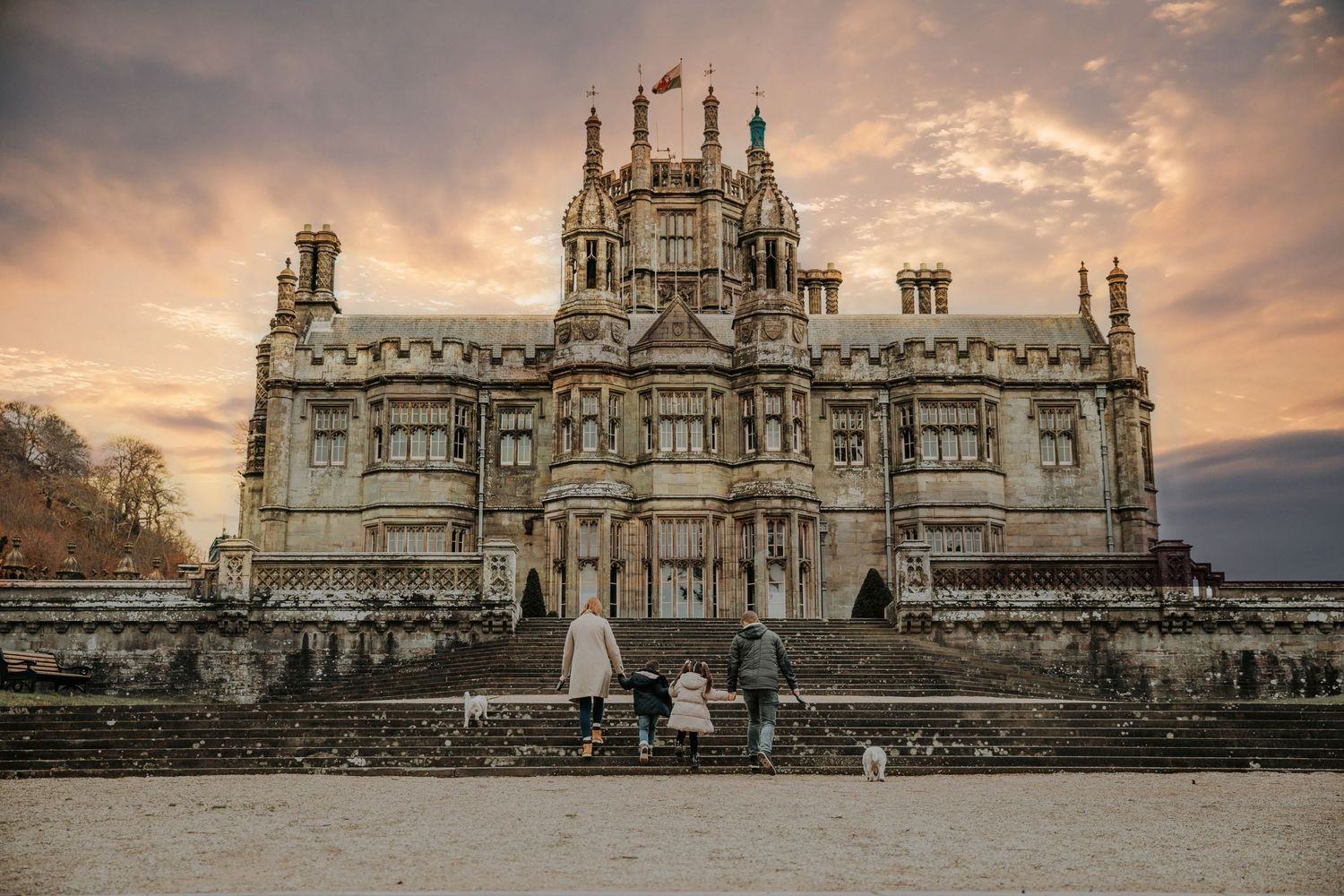 Family with dog standing before a grand historic castle at sunset with dramatic cloudy sky.