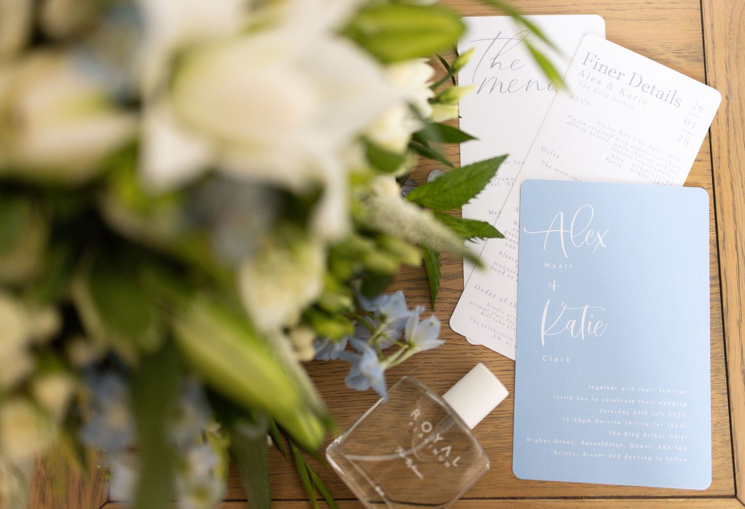 Wedding invitation suite with delicate blue and white stationery pieces arranged with fresh greenery and floral details.