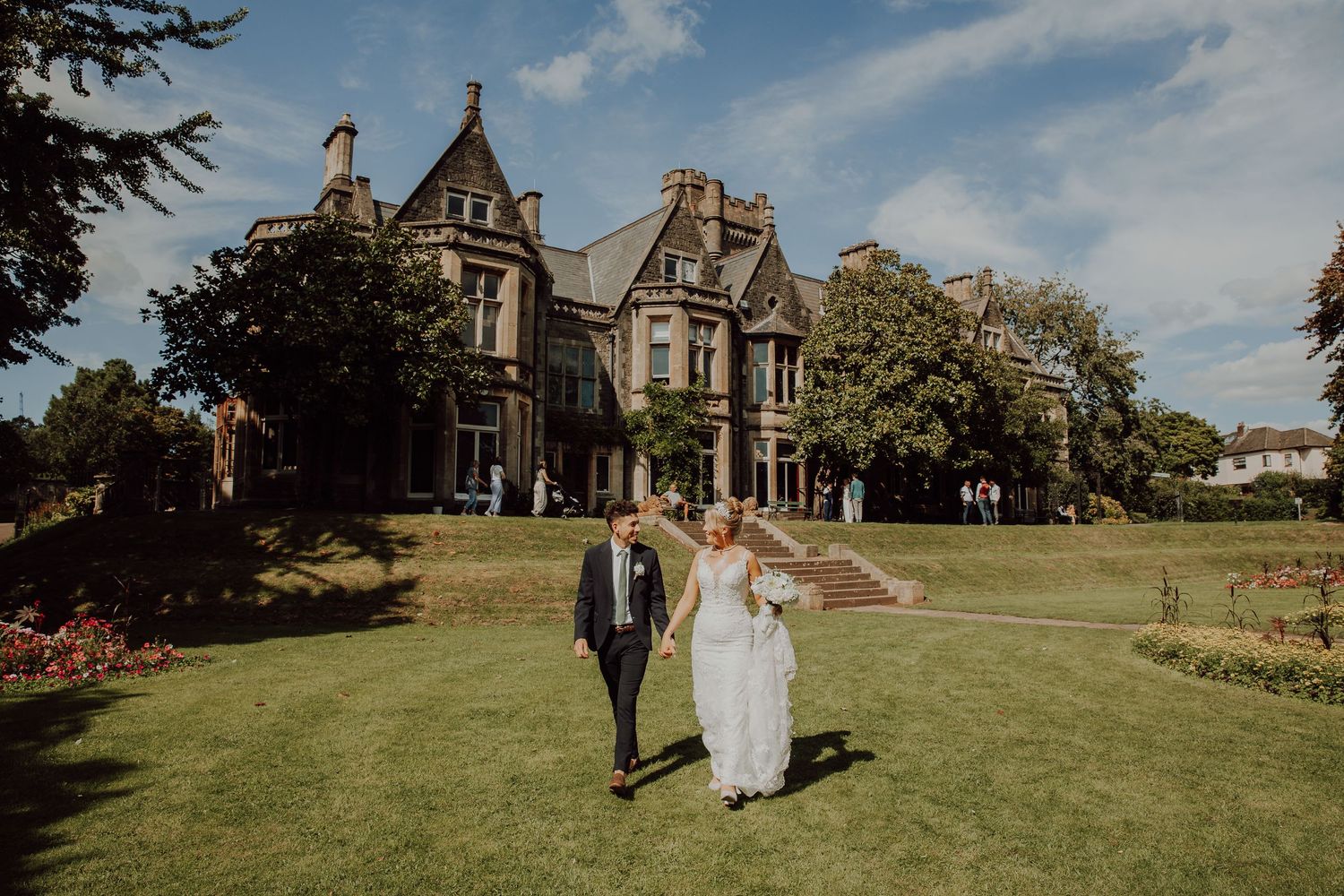Wedding couple walking across expansive lawn of historic stone mansion.