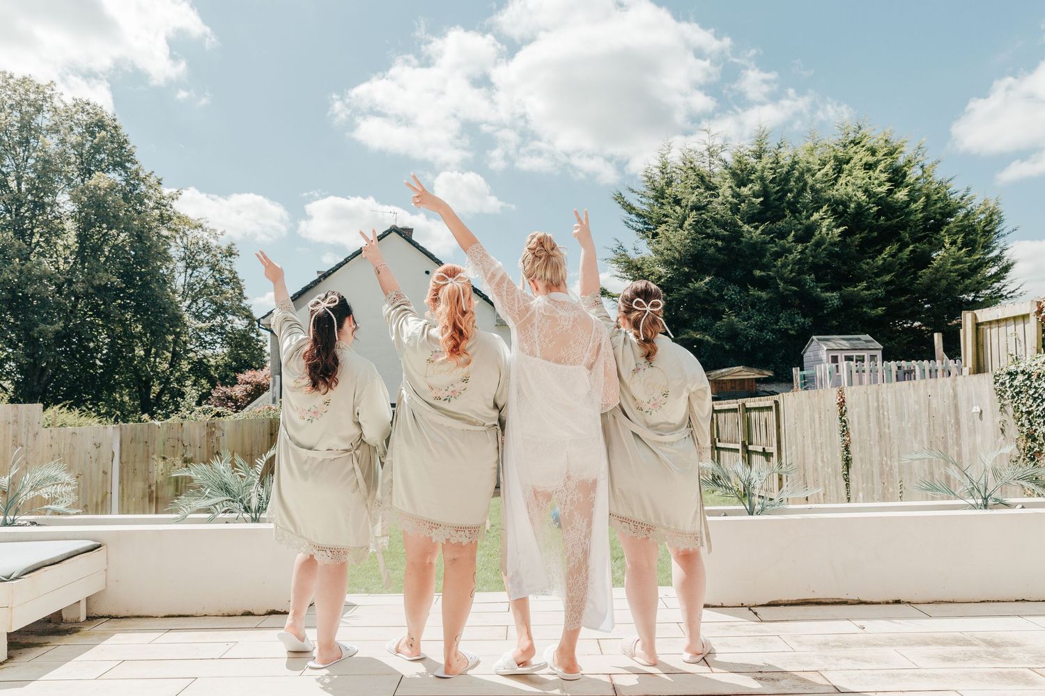 Bridesmaids in light colored dresses pose together on a sunny terrace.