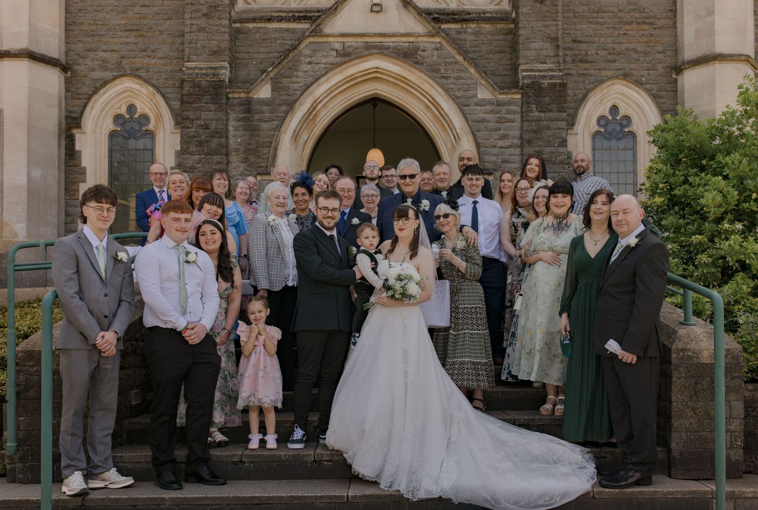Wedding group photo of bride and groom with family and friends on church steps.