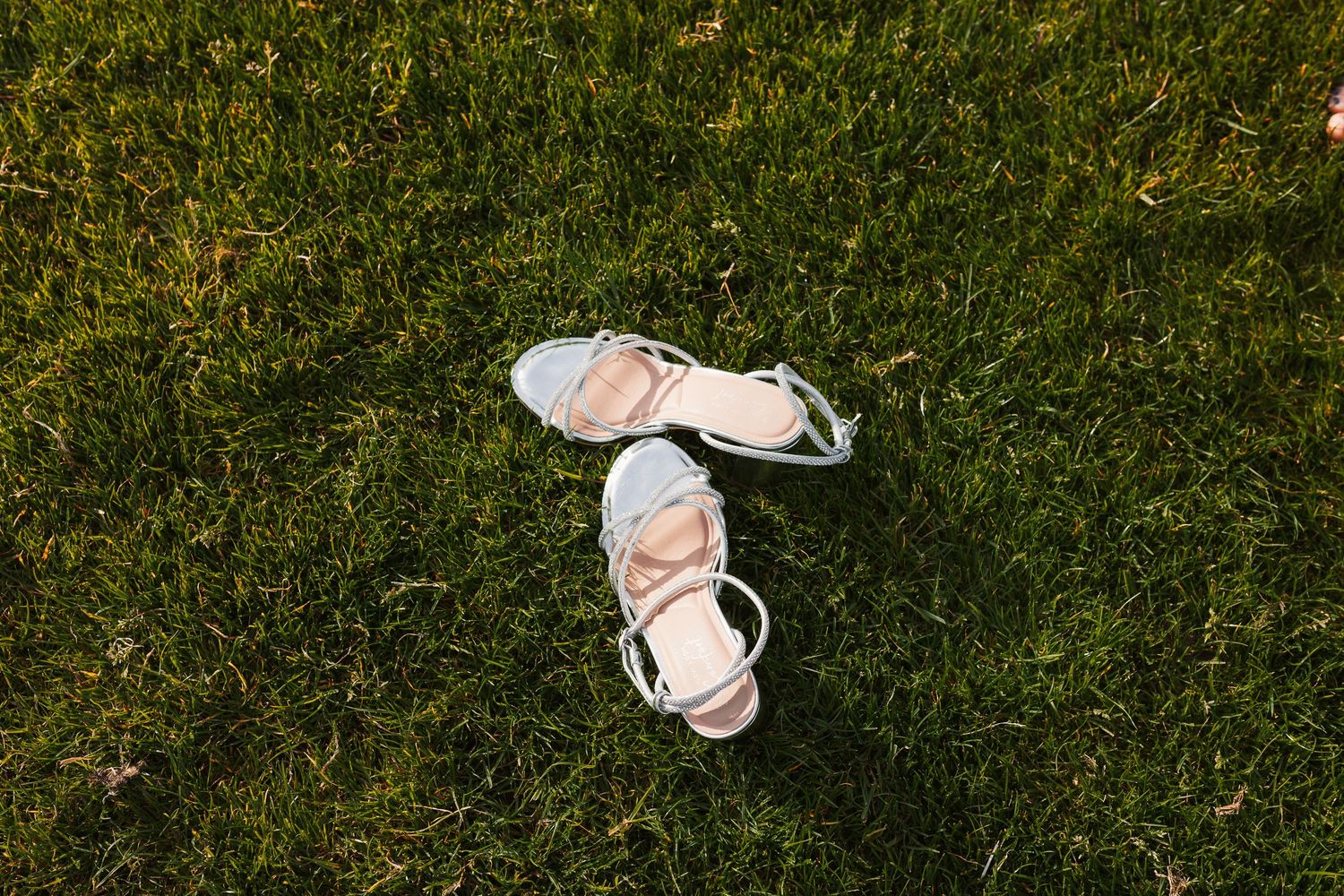 White strappy bridal heels resting on lush green grass at an outdoor wedding venue.