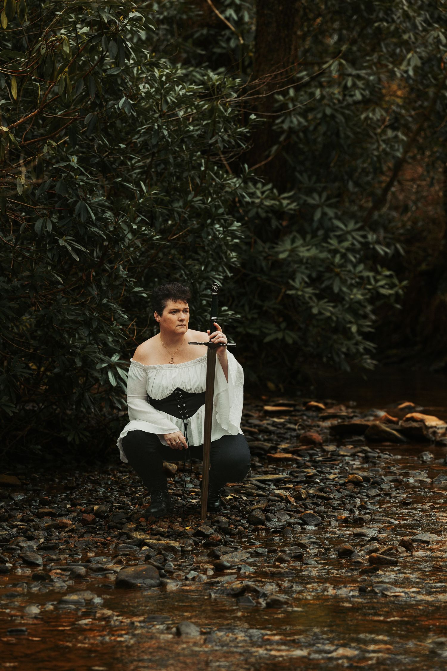 Figure in period costume poses with sword among autumn foliage and rocks.