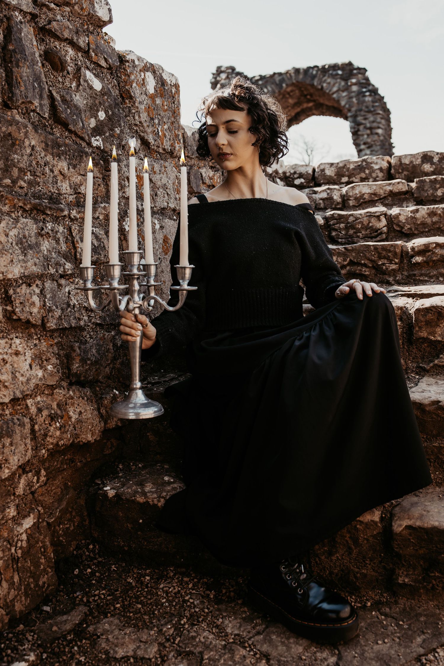 Gothic scene with silver candelabra and figure in black dress on stone ruins.