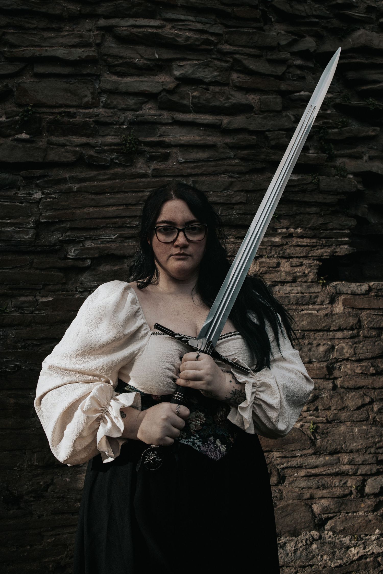 A medieval-inspired photoshoot featuring a sword against a stone wall backdrop.