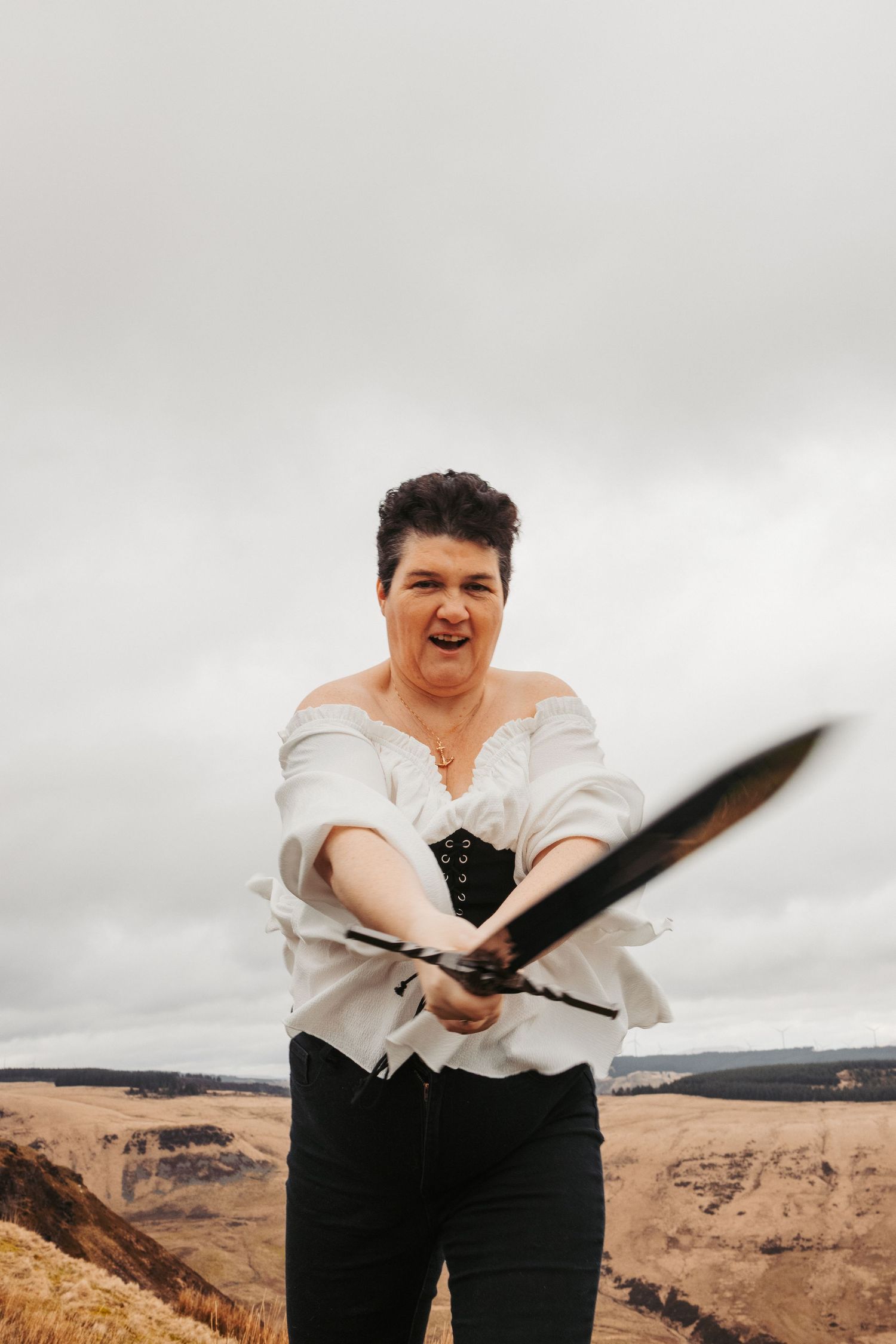 A person in medieval-inspired attire holds a sword against a cloudy mountain backdrop.