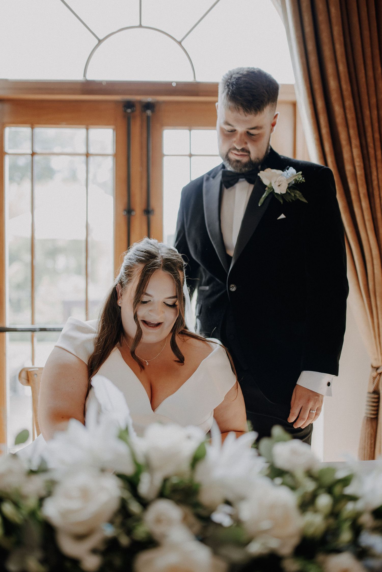 Elegant indoor wedding ceremony with white floral arrangements and warm lighting in a room with large windows.