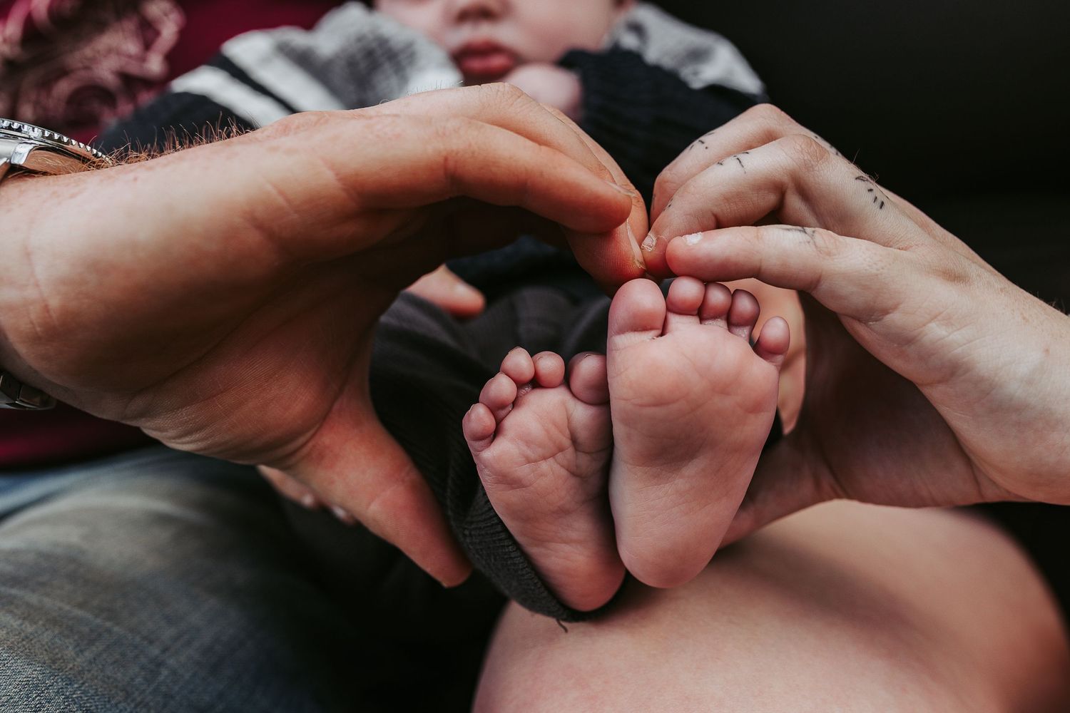 Two parents forming a heart shape with their hands around their newborn baby's tiny feet.