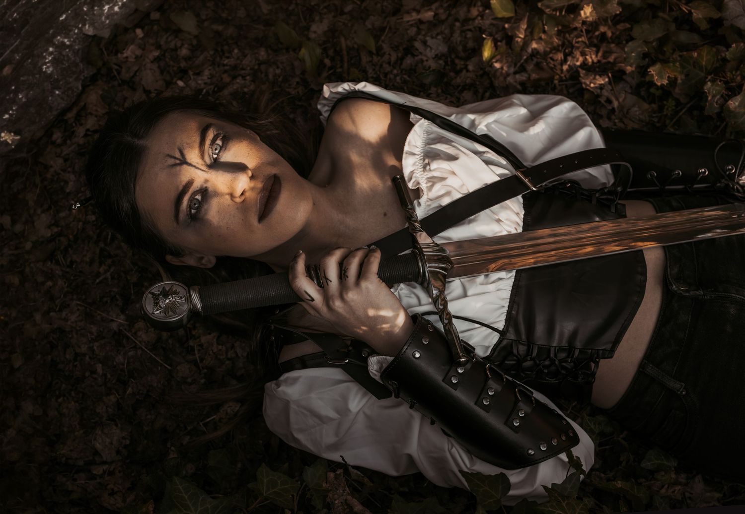Dramatic portrait of person in period costume lying on dark ground with sword.