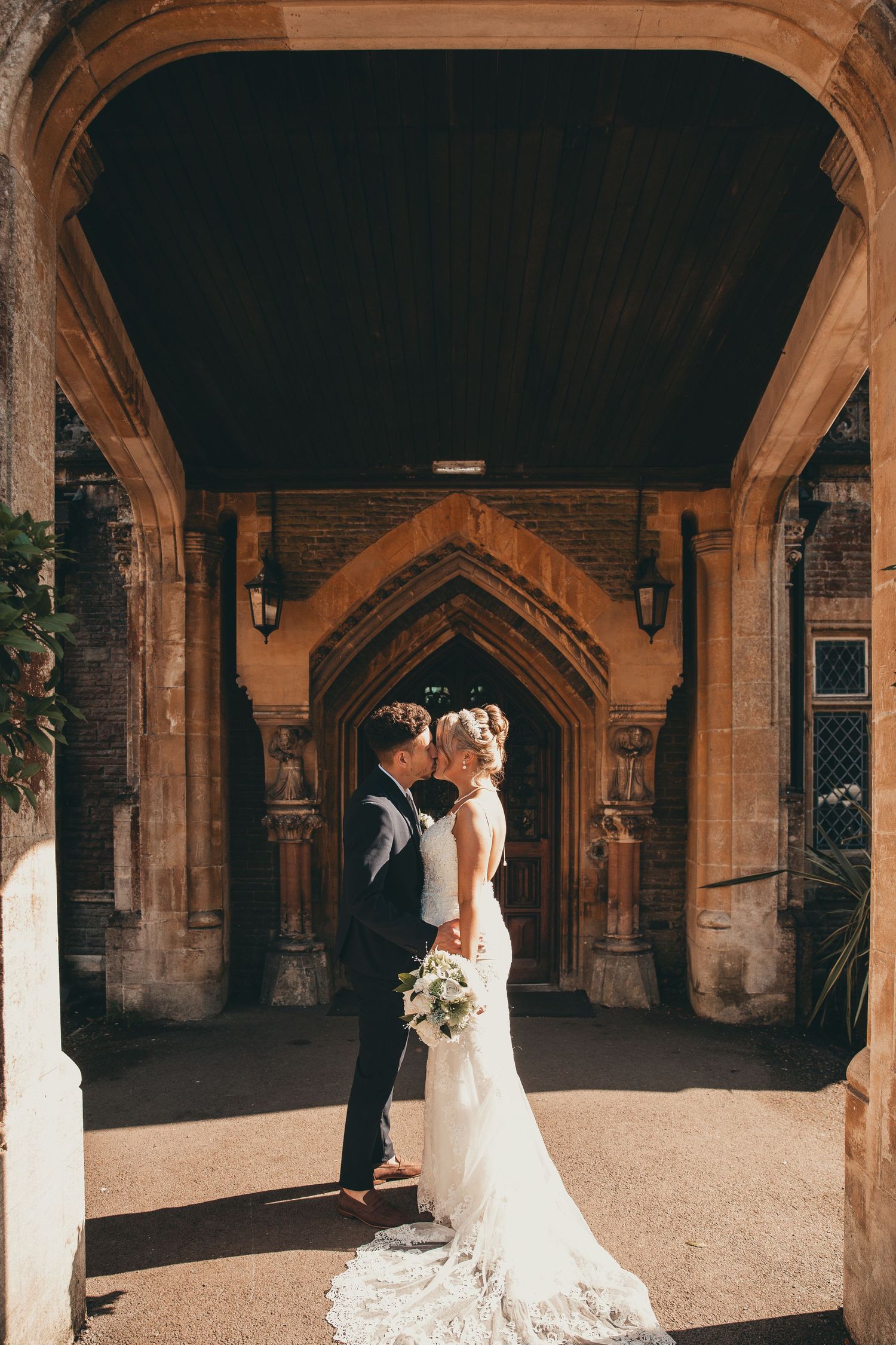 Elegant wedding portraits under gothic stone archways with dramatic lighting.