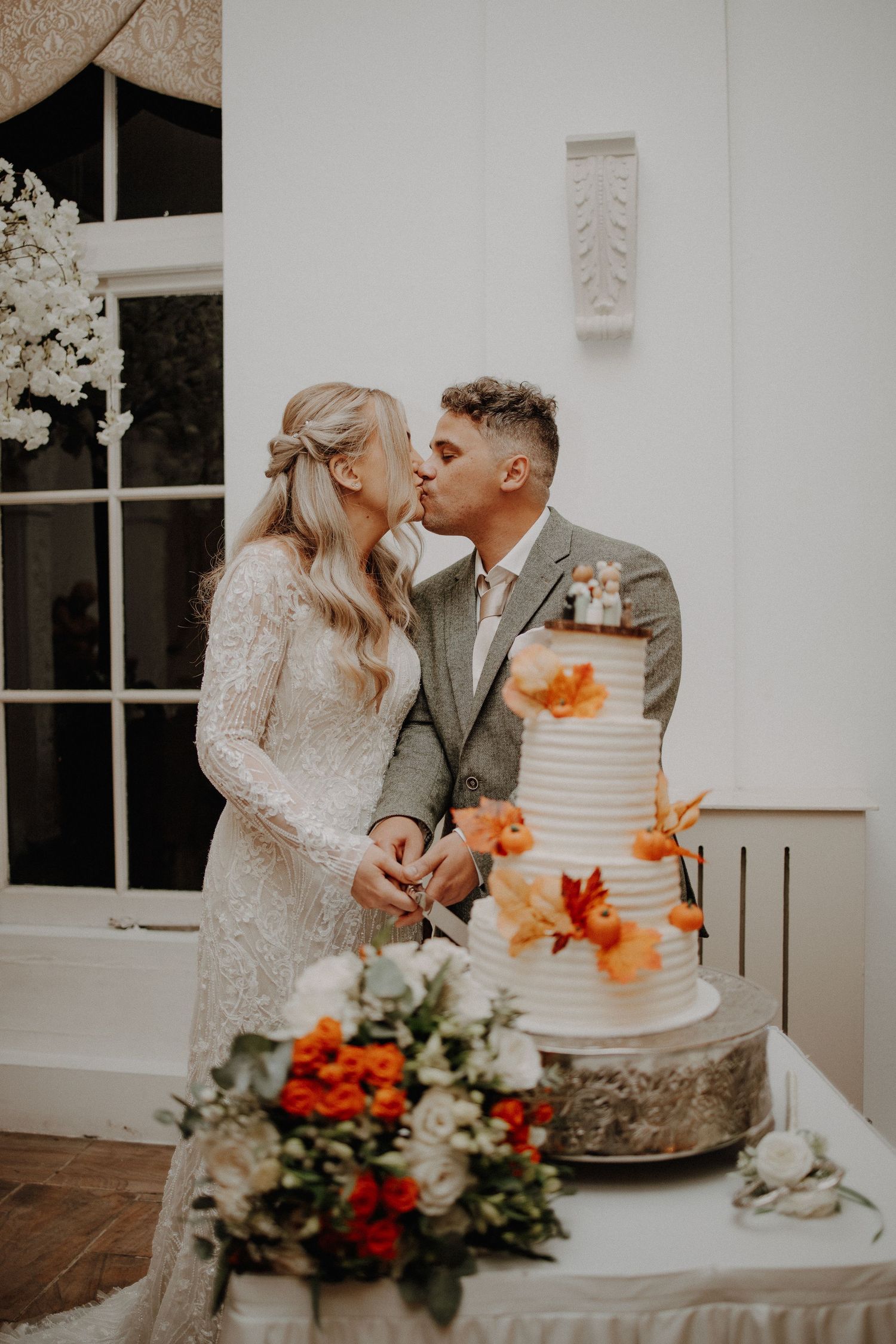 Couple sharing intimate moment while cutting their white wedding cake decorated with orange flowers.