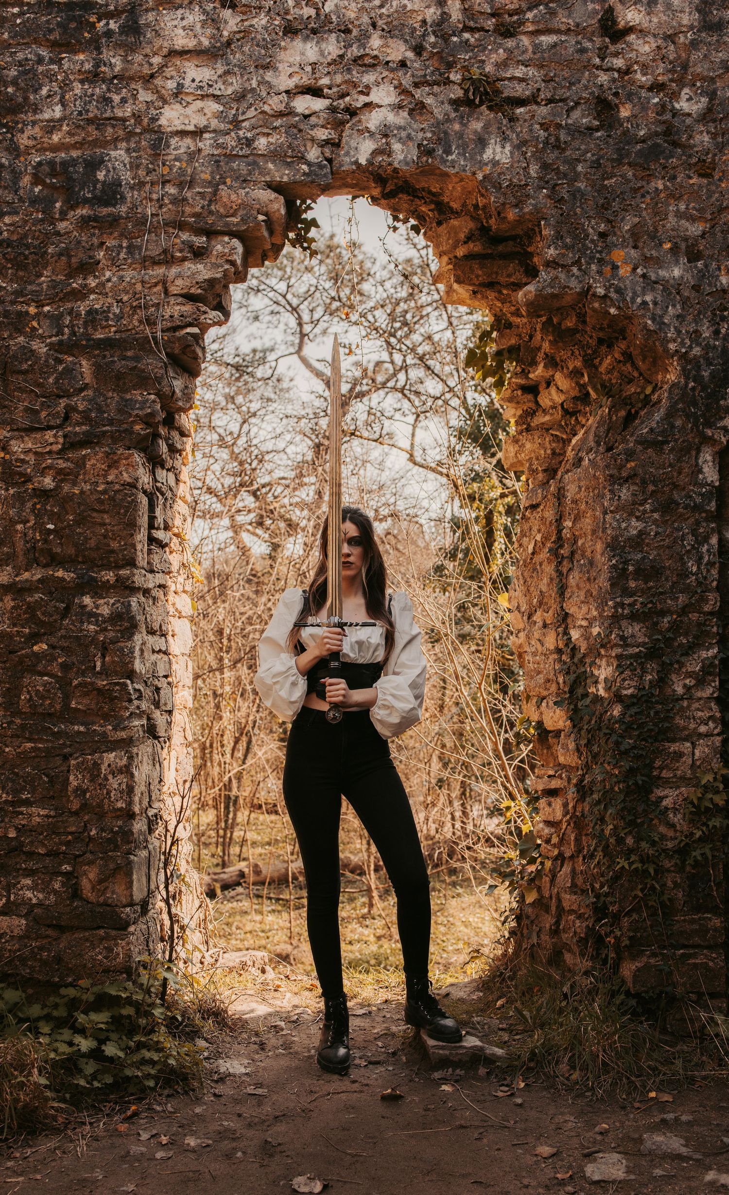 A silhouette stands in an ancient stone archway during golden hour.