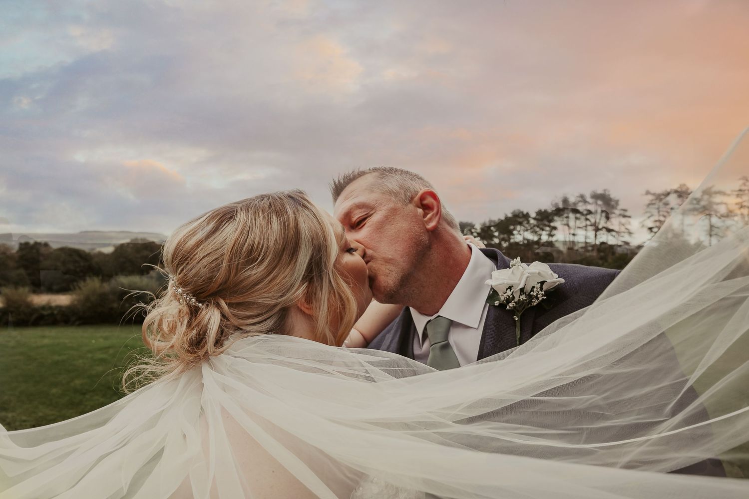 Romantic sunset wedding portrait with flowing veil creating dreamy silhouette.