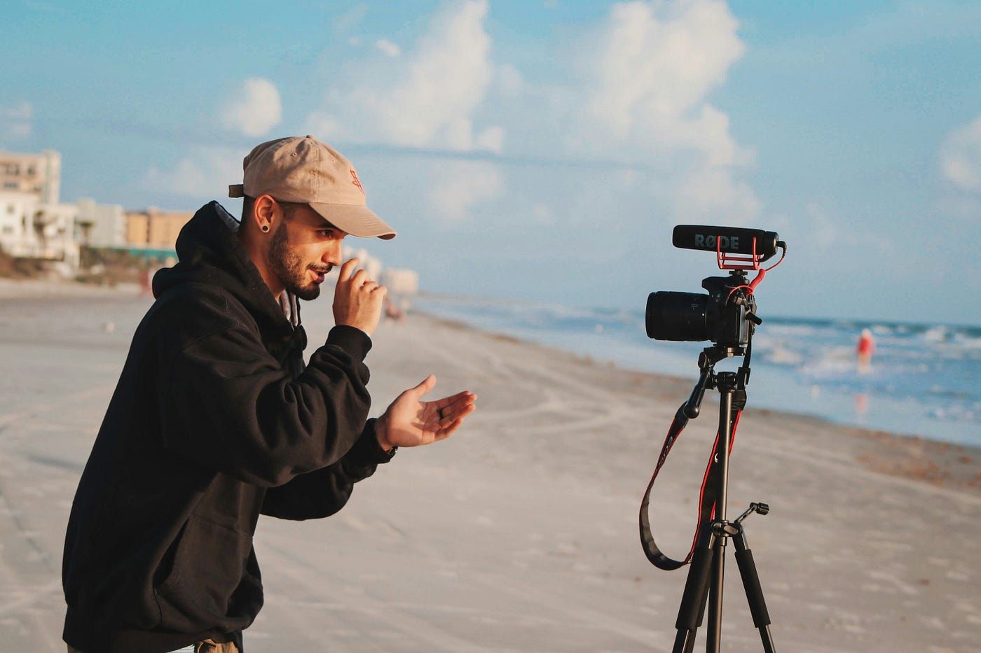 Photographer with camera and hat working on beach during sunset.