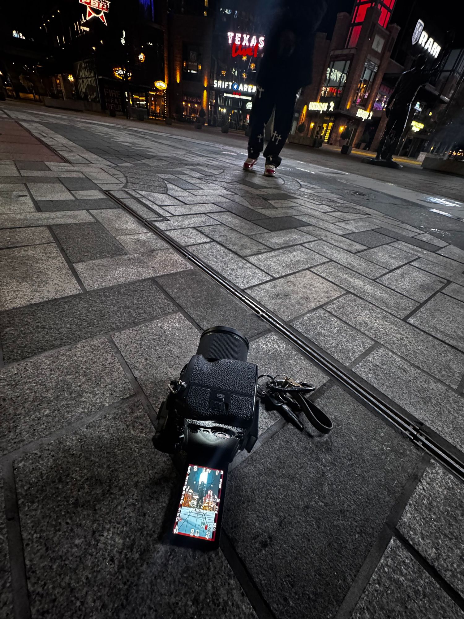 Urban street scene at night with electronic device visible in foreground.