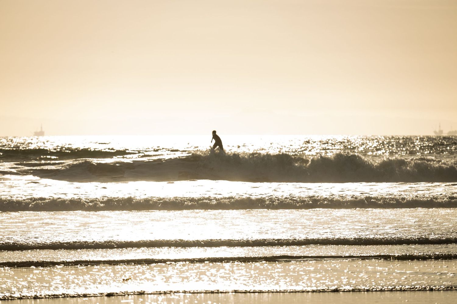 Silhouette of a surfer riding a wave during golden sunset with shimmering light on the ocean surface.