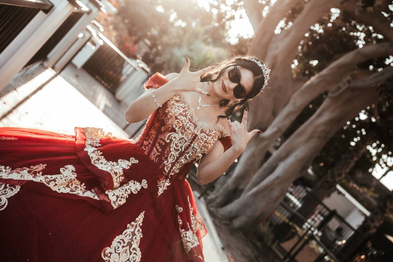 Young woman in red and white embroidered dress twirling outdoors in golden sunlight near a tree.