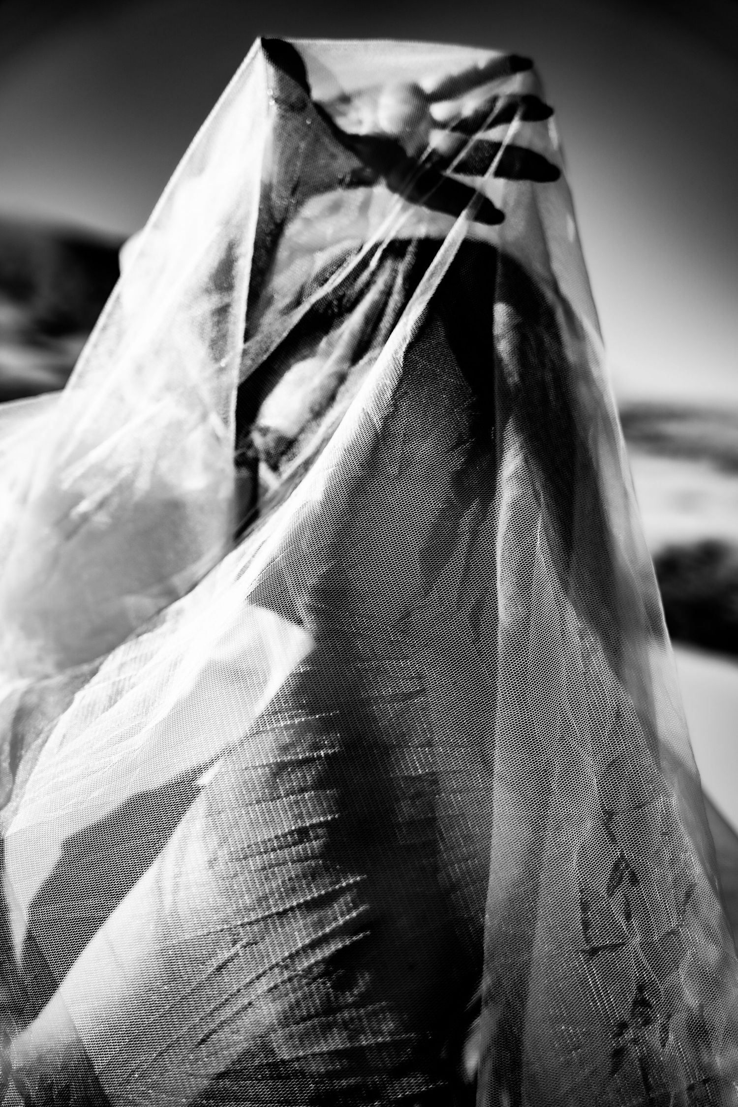 Black and white artistic photo of a person completely draped in translucent plastic sheeting outdoors.
