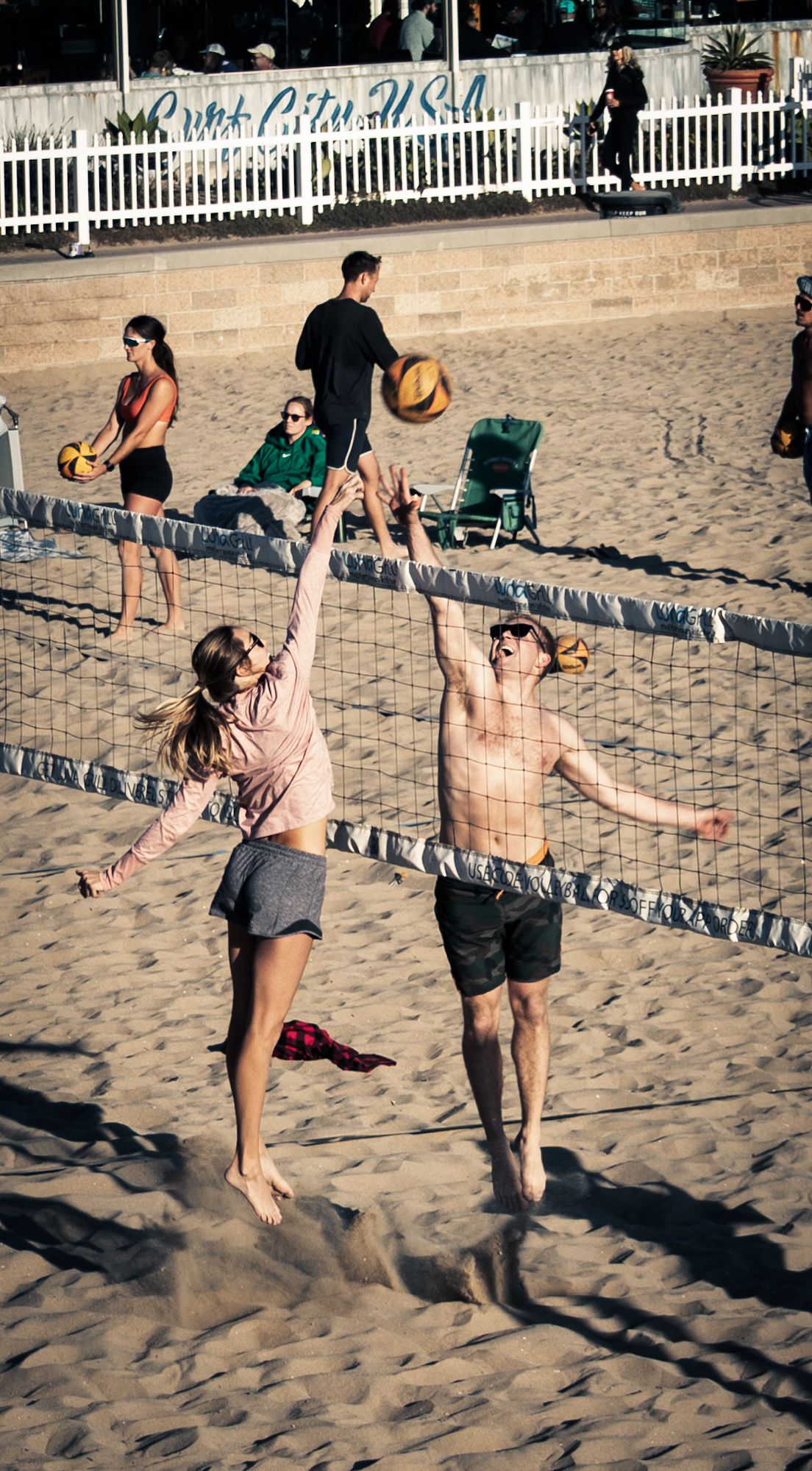 Two players competing at a beach volleyball net on sandy shore with spectators in the background.