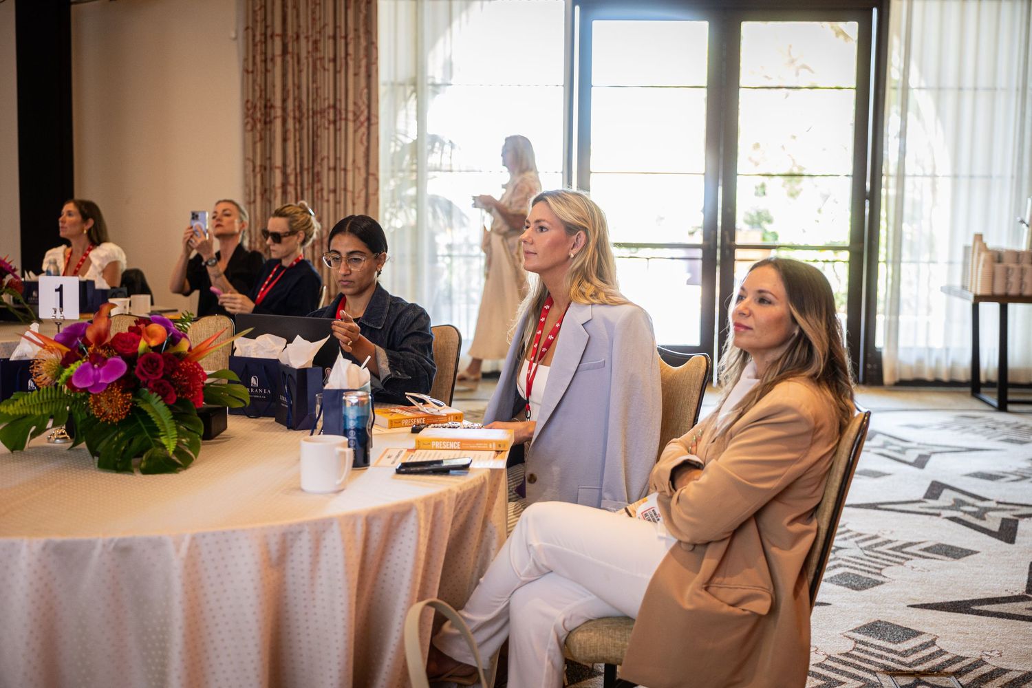 Attendees seated at a round table during a daytime conference event in an elegant hotel ballroom.